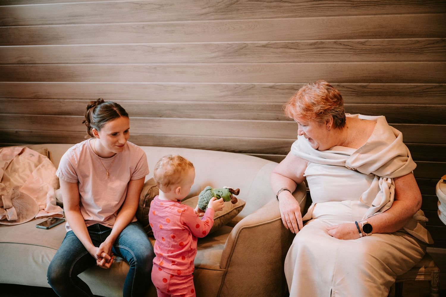 A tender family moment shared on a cozy brown couch as they interact with a small child in pink.