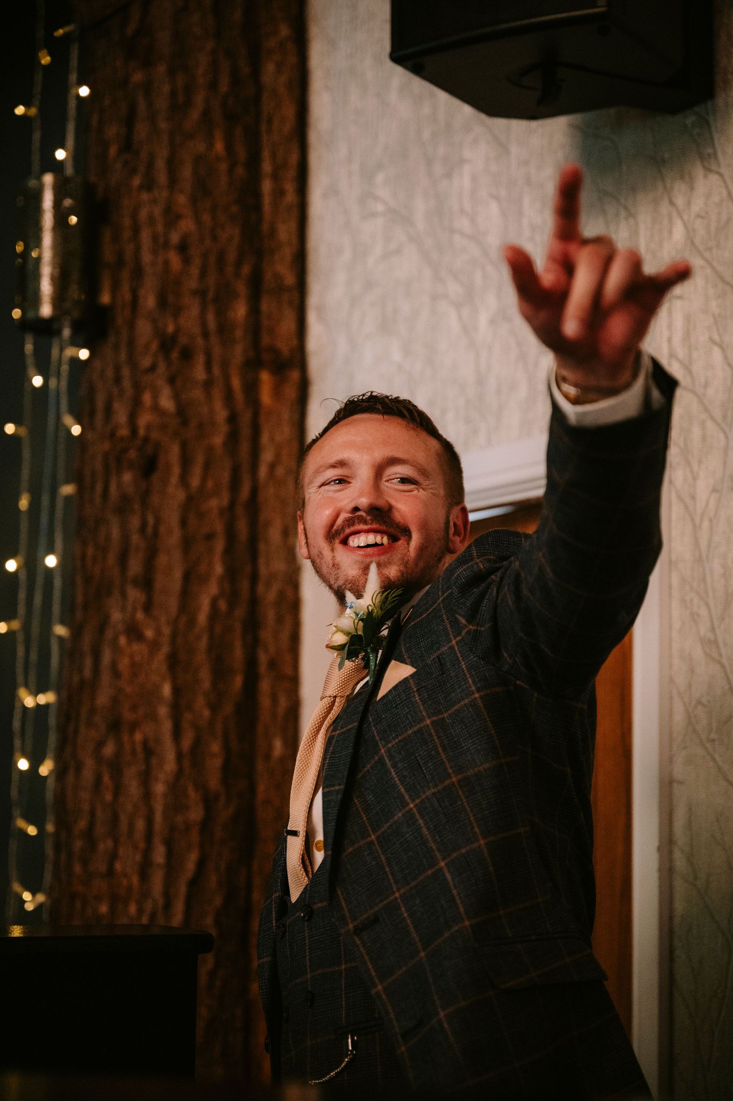 Person in plaid suit jacket celebrates enthusiastically against a backdrop of twinkling lights.