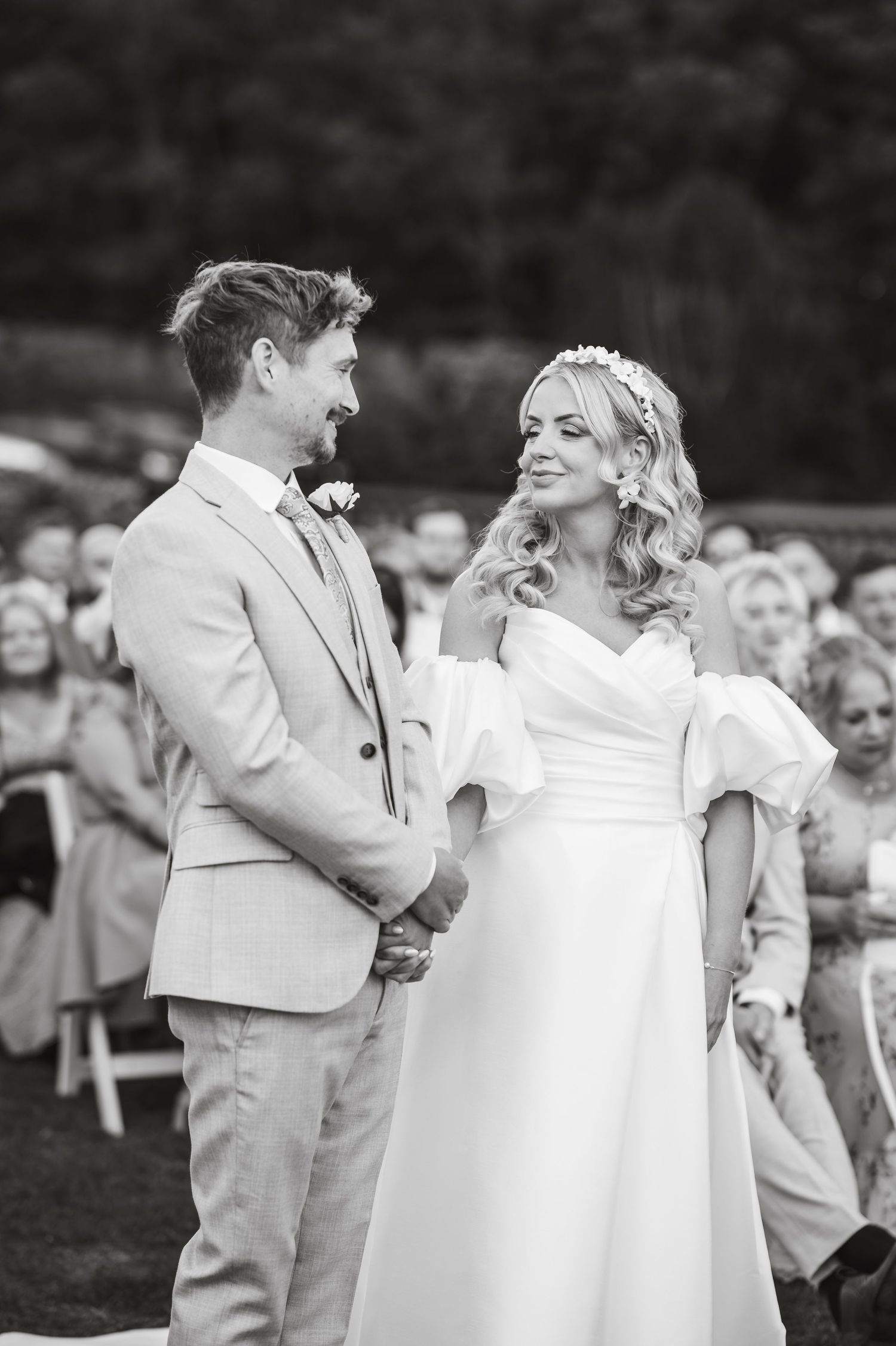 A joyful black and white wedding ceremony moment showing the couple laughing together outdoors with guests in background.