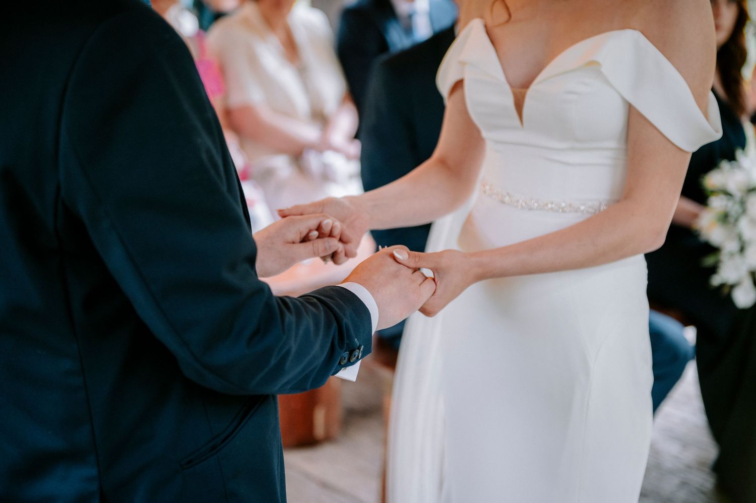Close-up of hands during wedding ring exchange ceremony in white dress and navy suit.