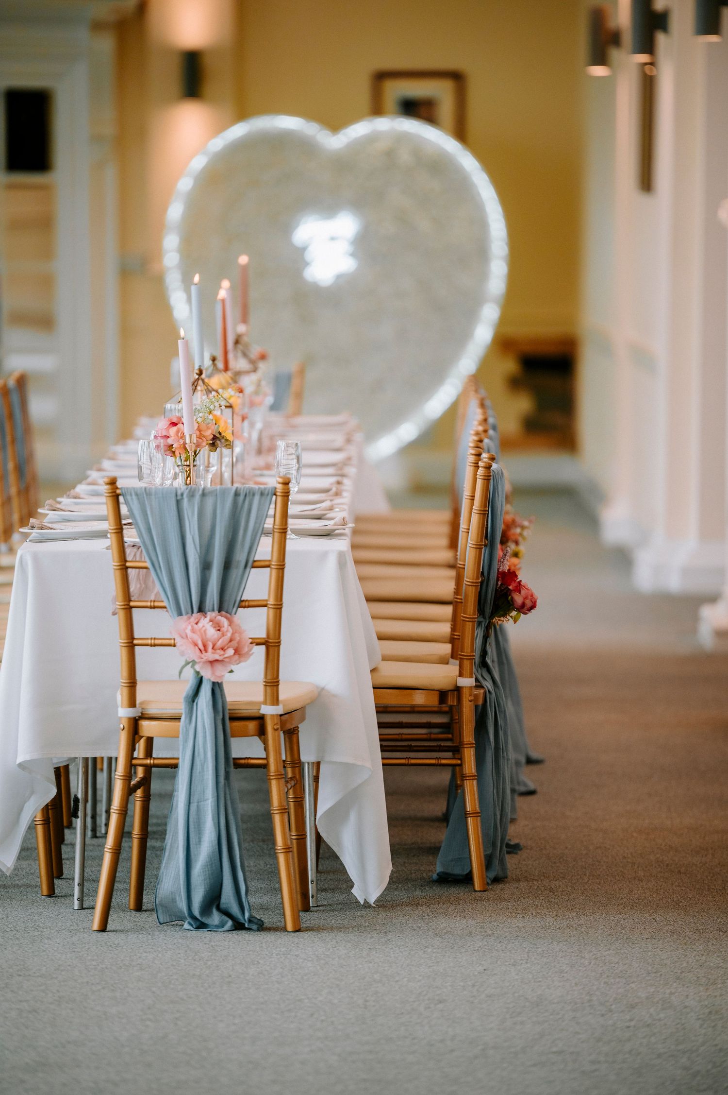 Wedding reception setup with white and dusty blue chair decorations in an elegant indoor venue.