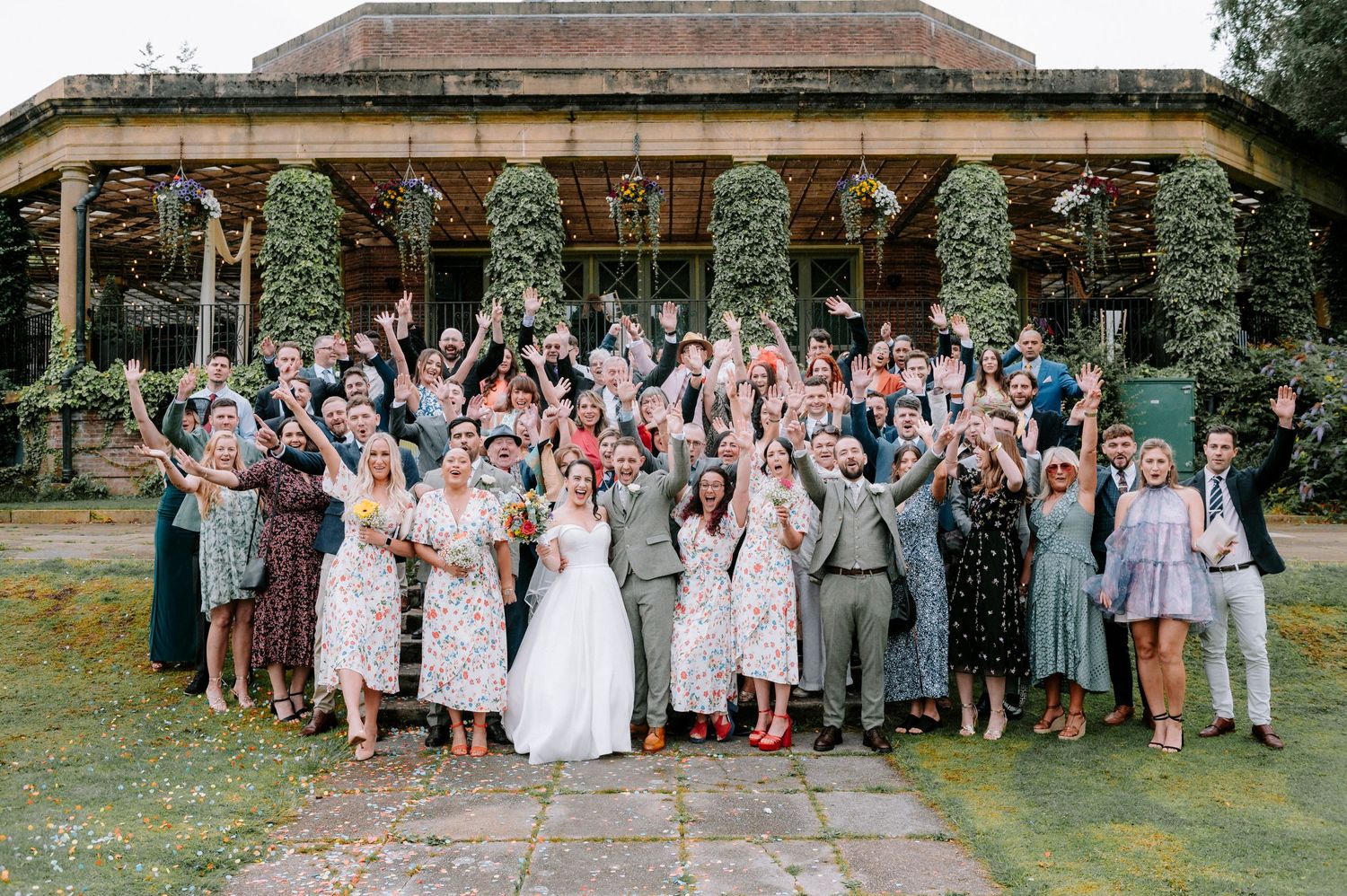 Large wedding party group photo taken outdoors in front of a rustic venue.