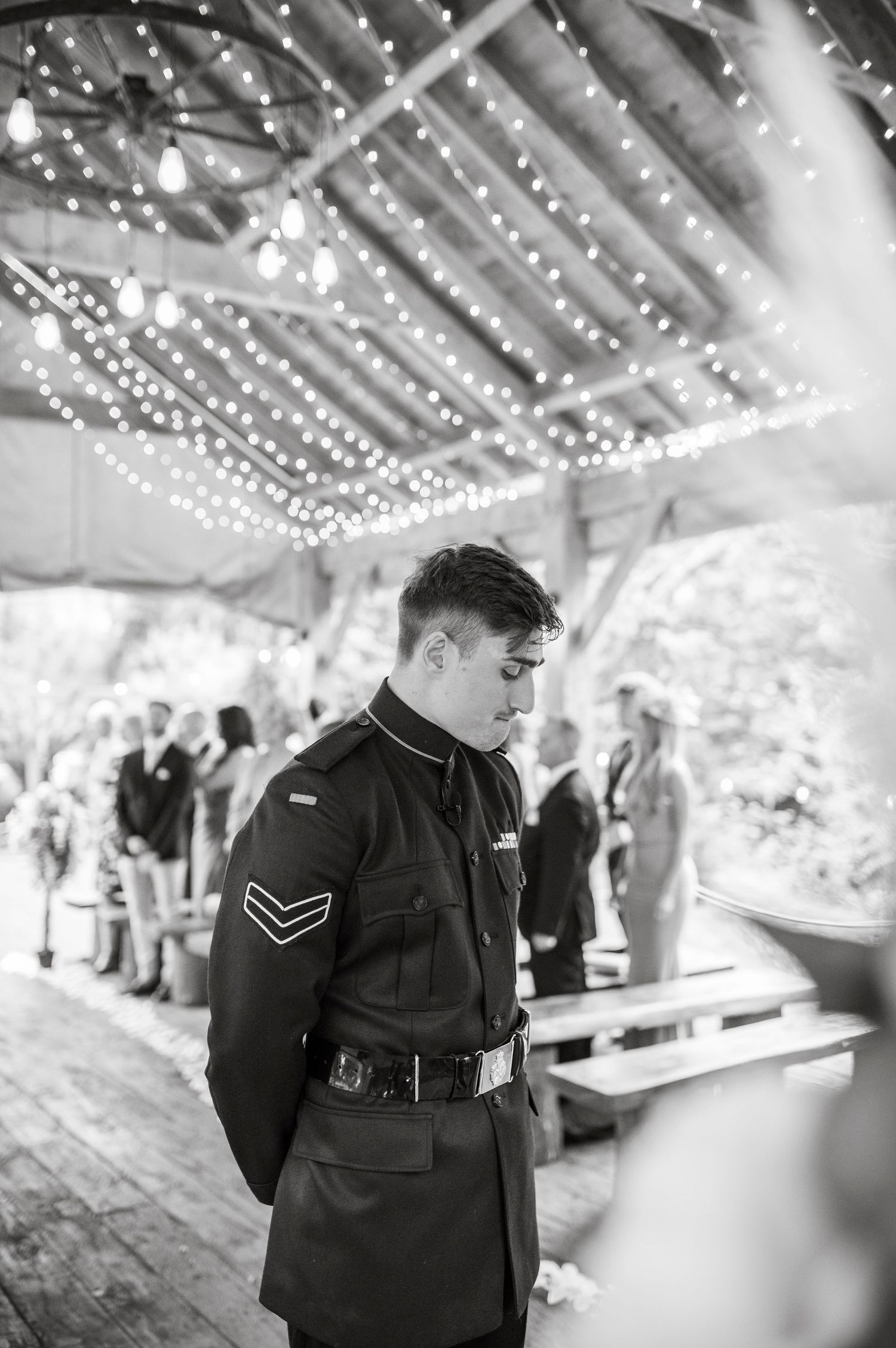 Military personnel stand under twinkling string lights at an elegant indoor reception venue.