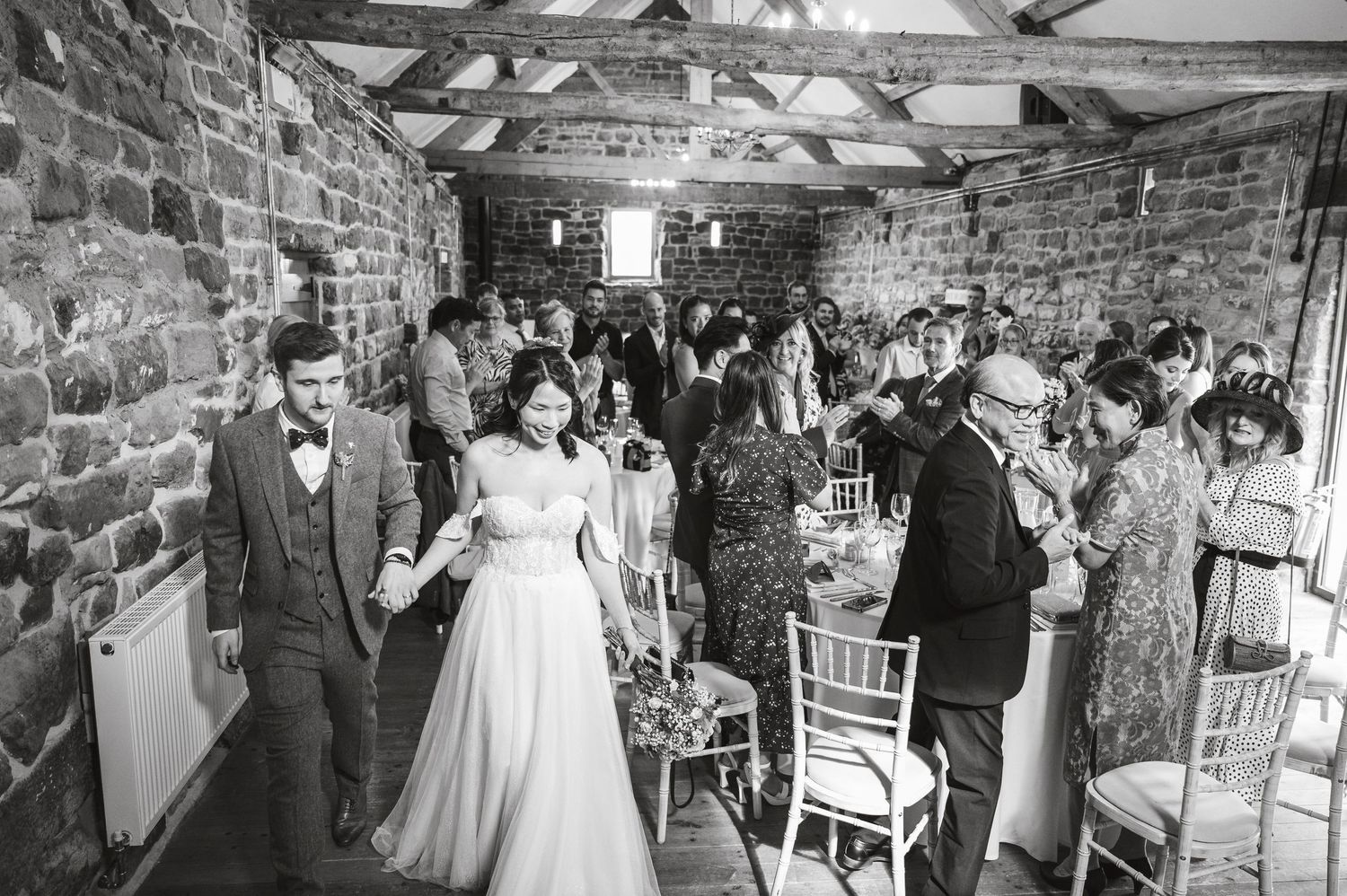 Black and white photo of wedding celebration in historic stone barn with elegant decor and dancing guests.