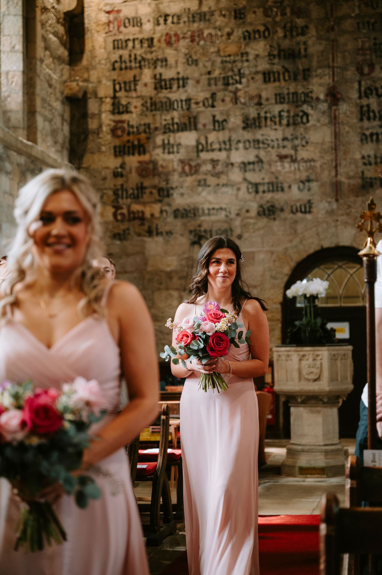 Bridesmaids in pink gowns holding pink and white bouquets during church ceremony.
