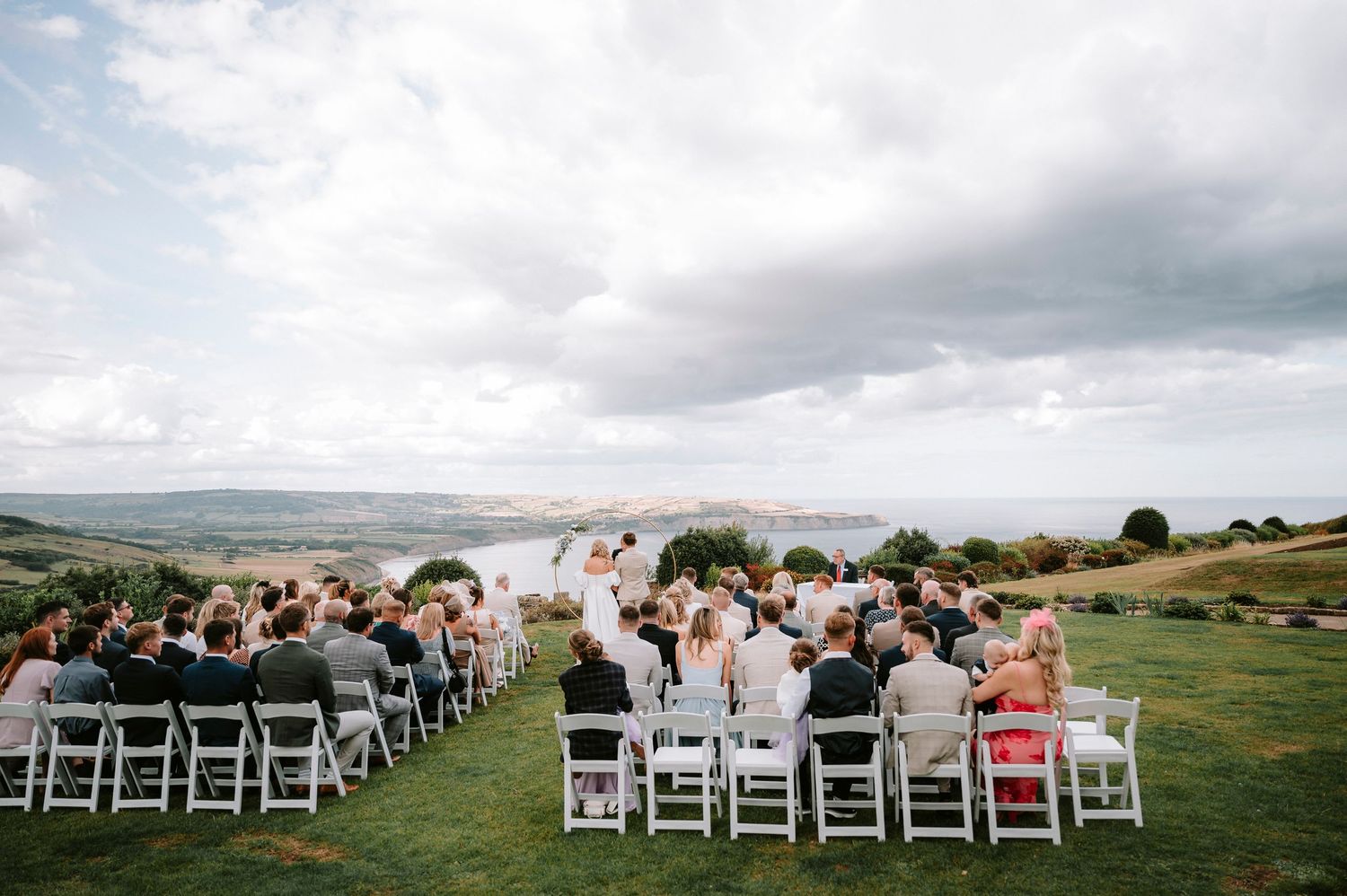 Wedding ceremony setup with white chairs arranged on a grassy hillside overlooking a scenic landscape.