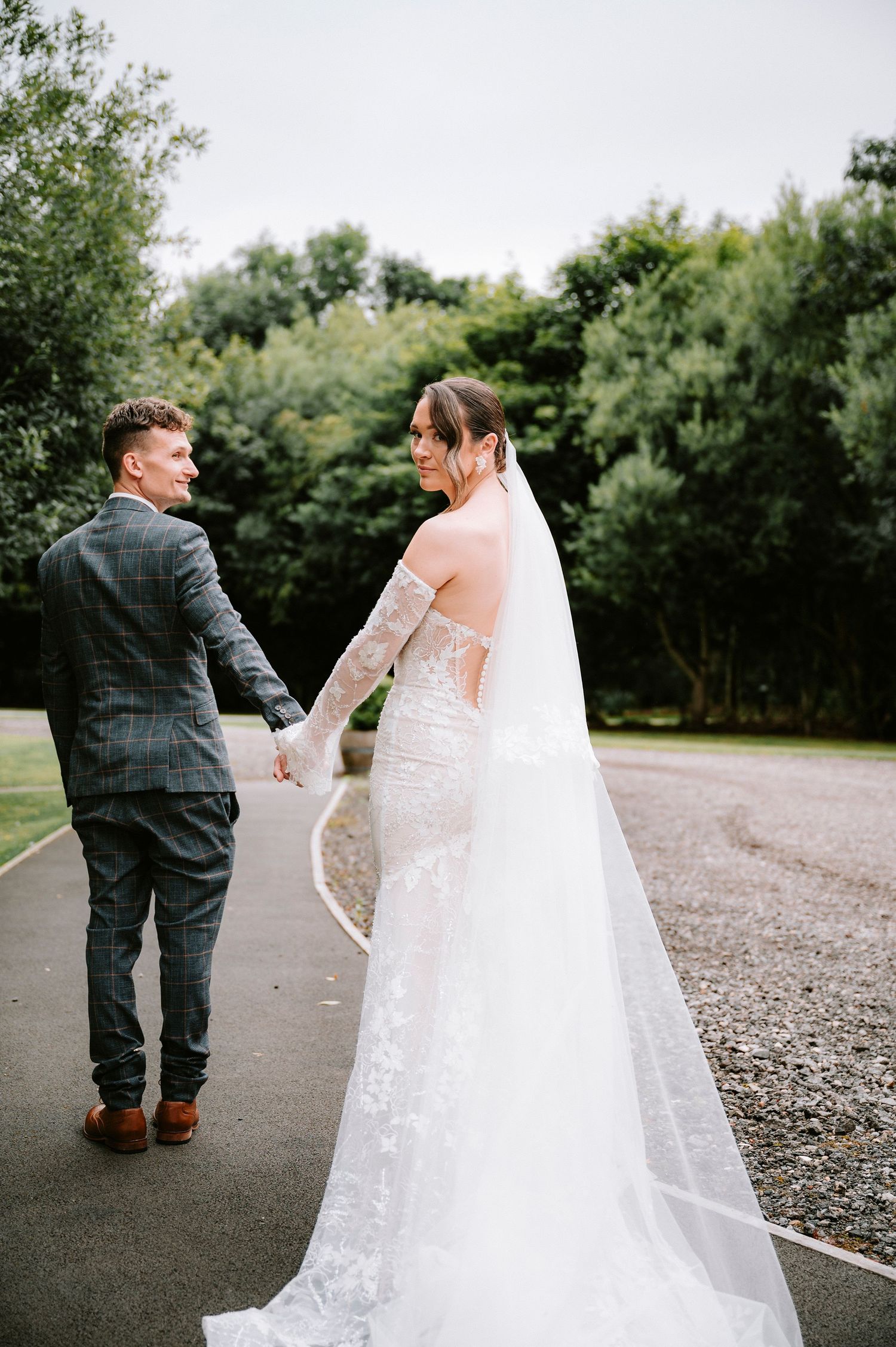 Couple walking together on a gravel path surrounded by trees and greenery.