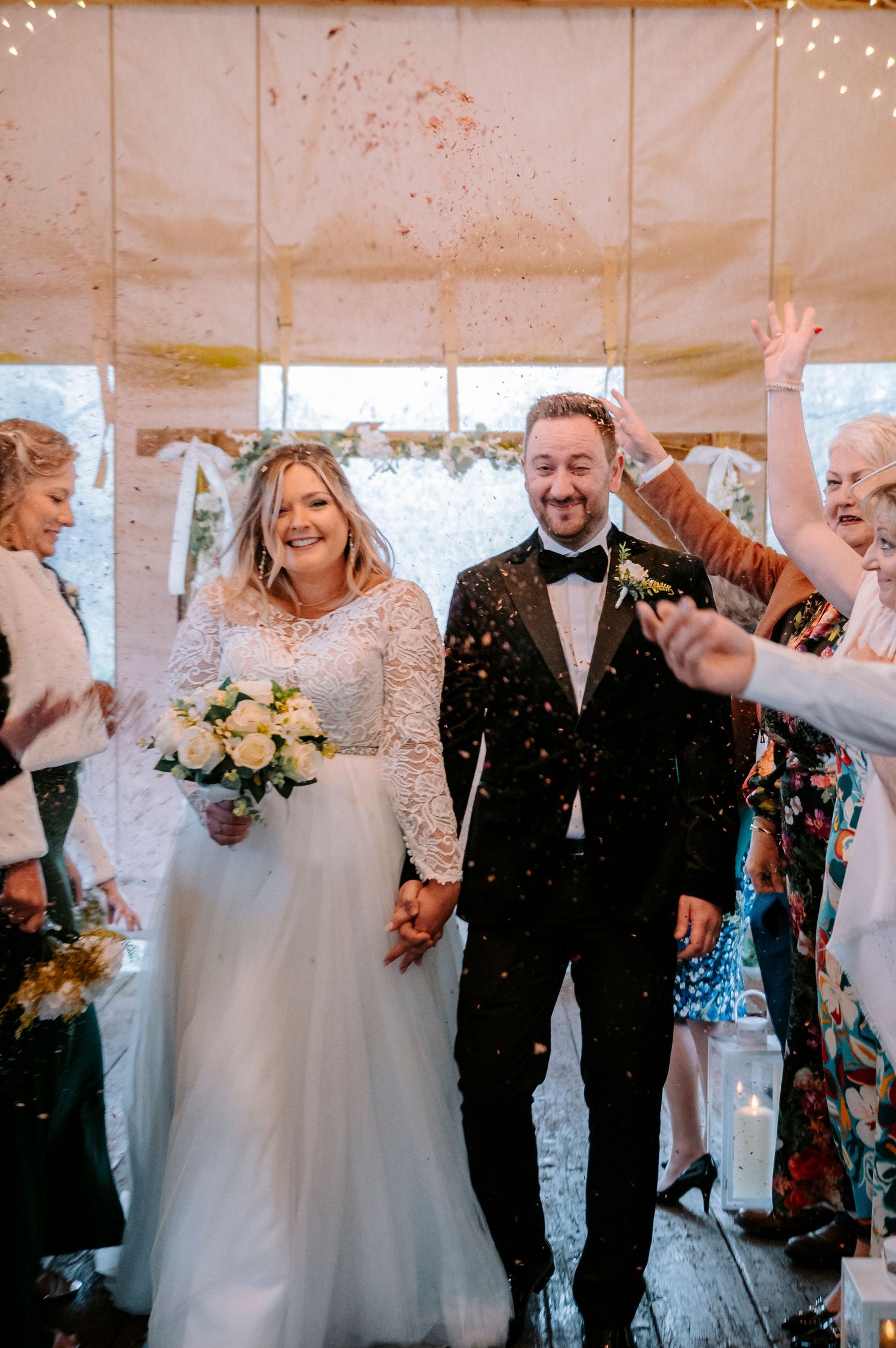 Joyful wedding celebration with confetti in a rustic barn setting with string lights.