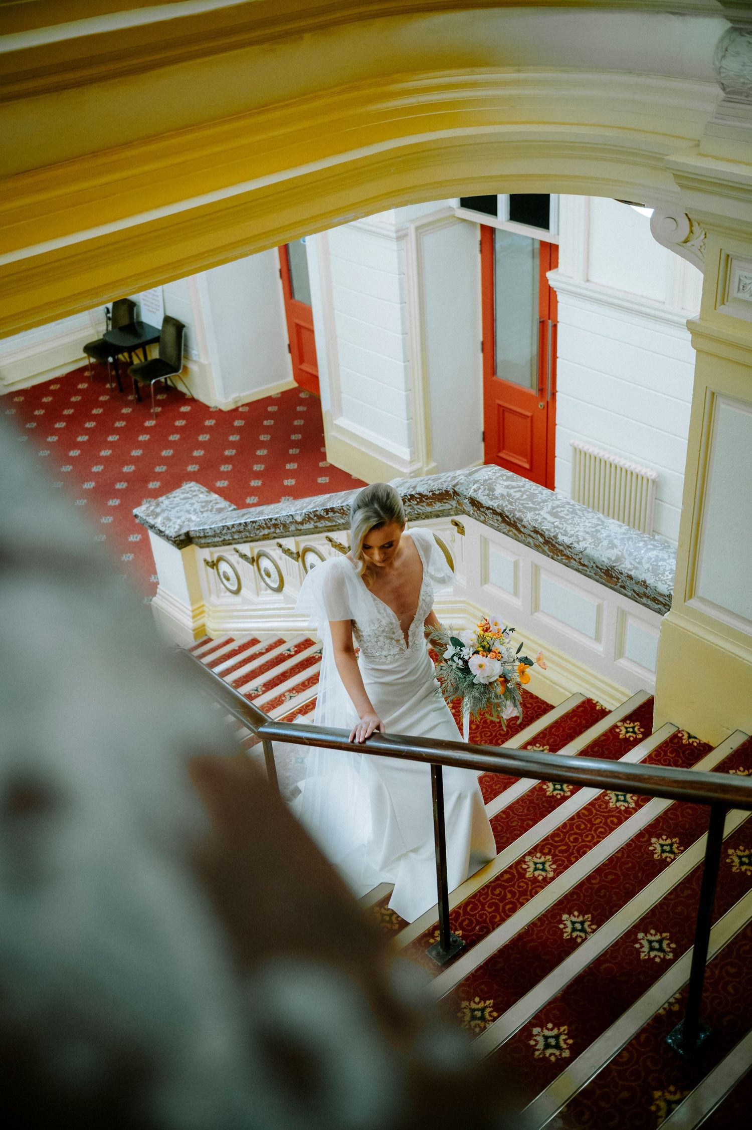 Wedding dress photographed on red carpeted stairs with ornate white railings.