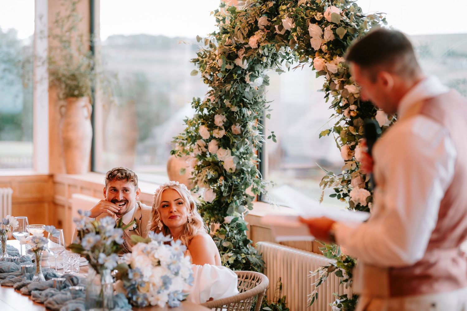 Wedding reception table decorated with floral arch and guests enjoying the celebration.