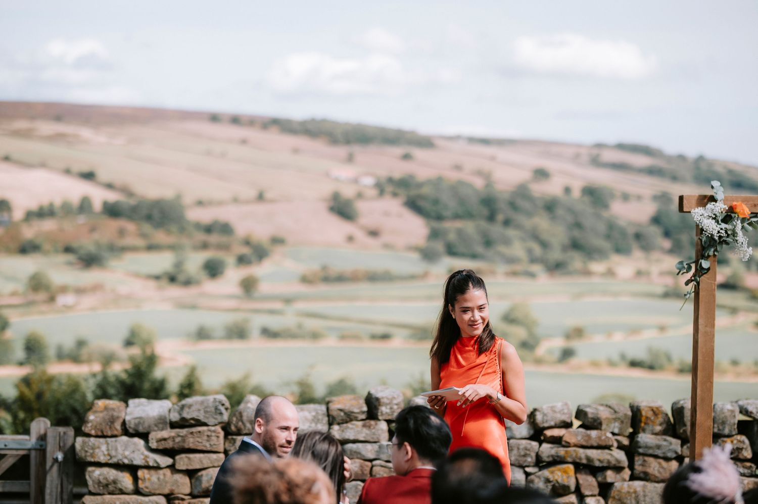 Rolling countryside hills and stone walls create a scenic backdrop for an outdoor wedding ceremony.