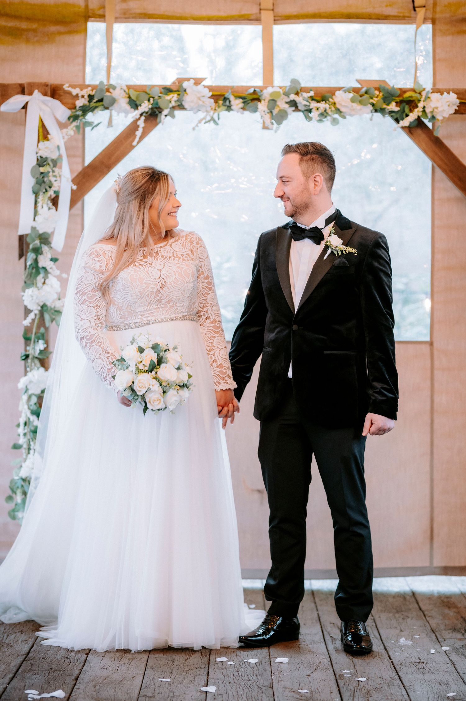 Wedding couple posing in a rustic wooden venue decorated with floral arrangements.