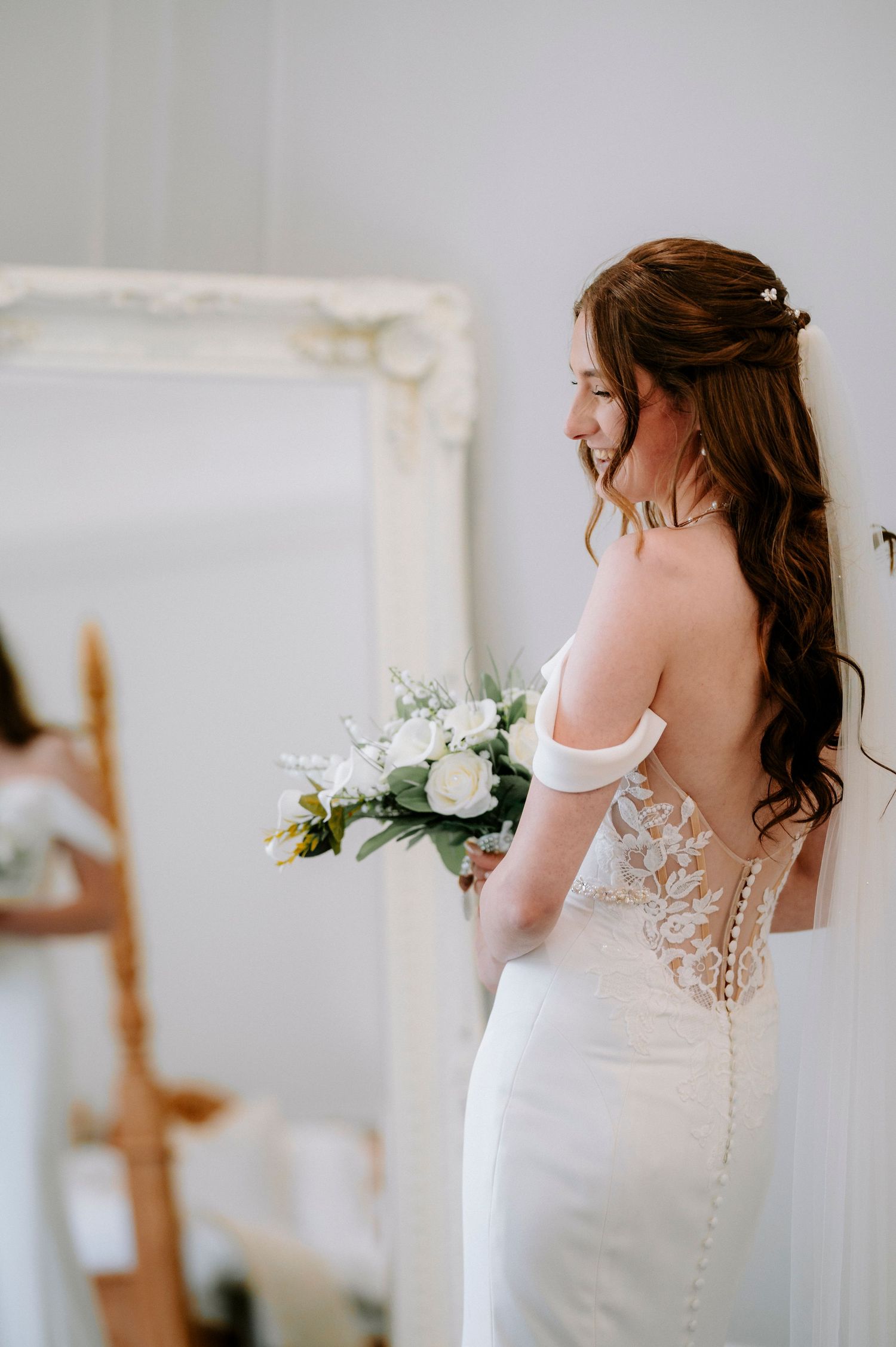 Close-up details of an elegant white lace wedding dress with buttons and floral bouquet.