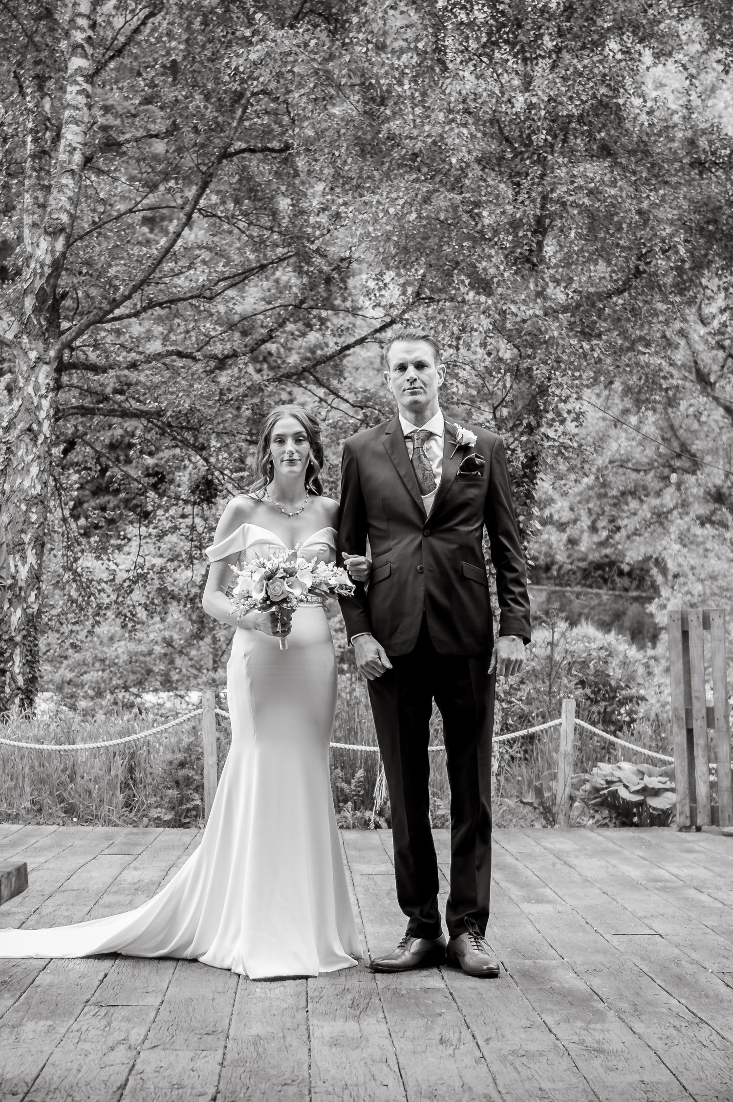 Black and white portrait on rustic wooden deck with natural foliage backdrop.