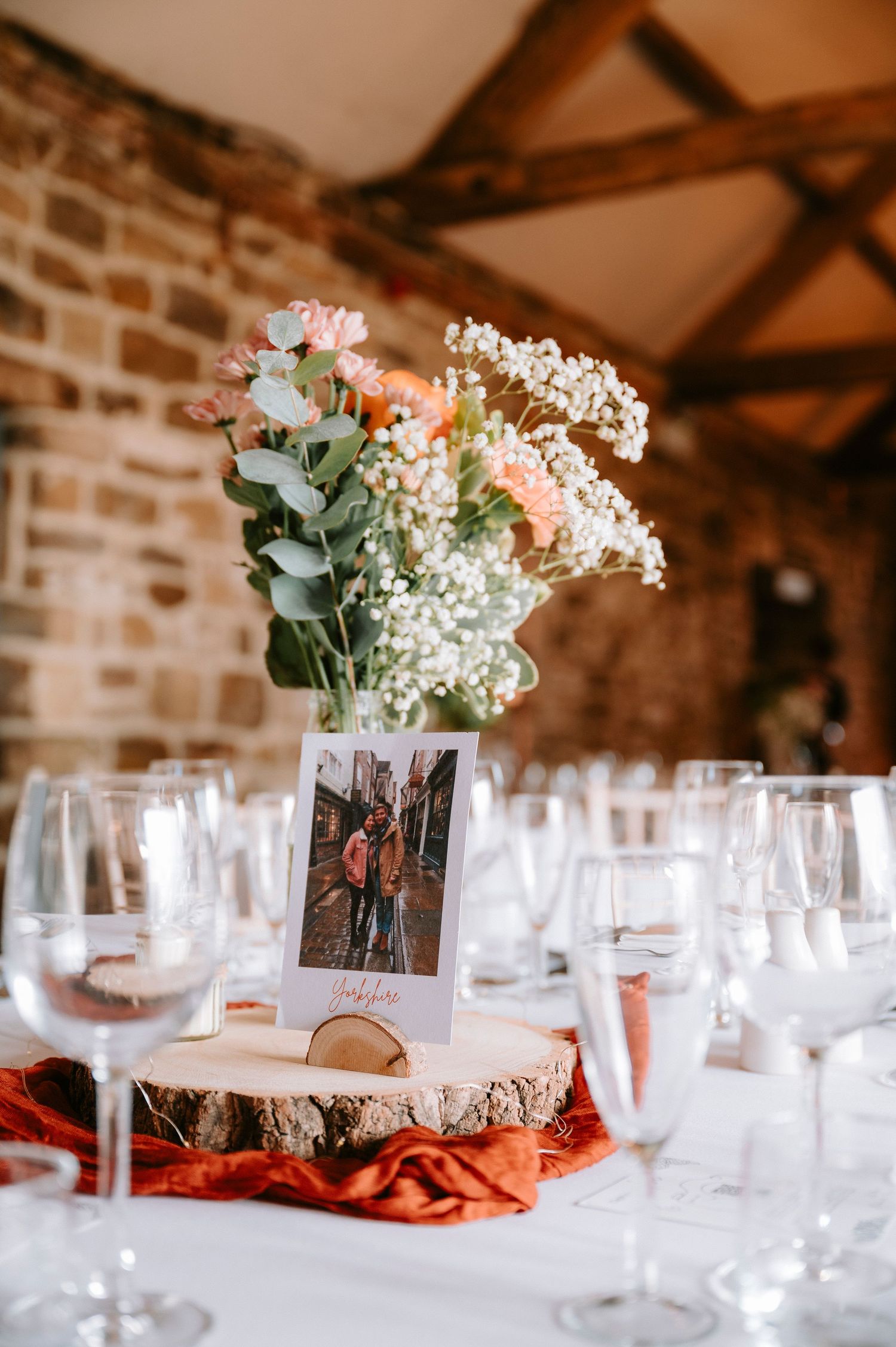 Elegant wedding reception table settings with white floral centerpieces and photo frames in a rustic barn venue.