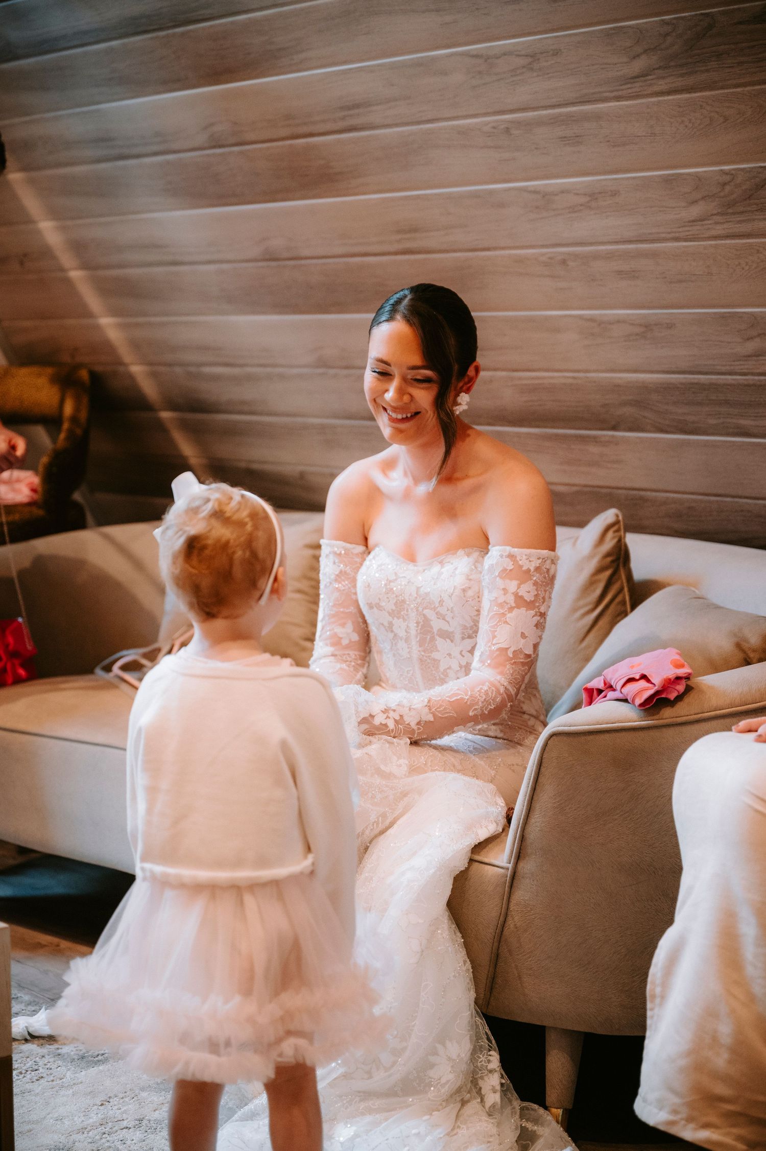 A bride in a beautiful lace gown shares a moment with a young flower girl in a tulle dress.