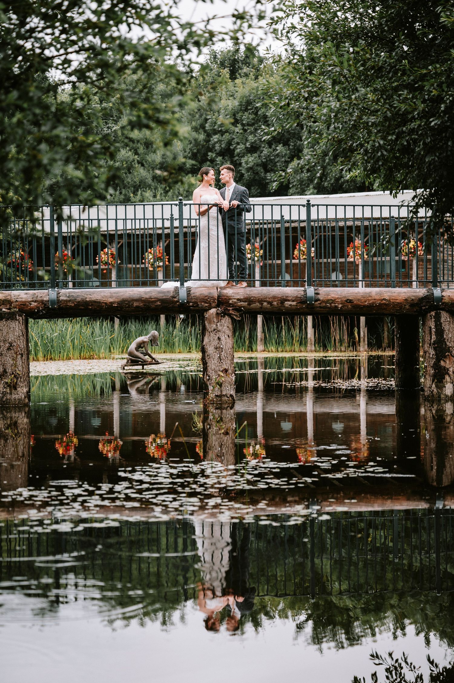 Serene waterfront wedding venue with wooden dock and lily pads reflecting in still water.