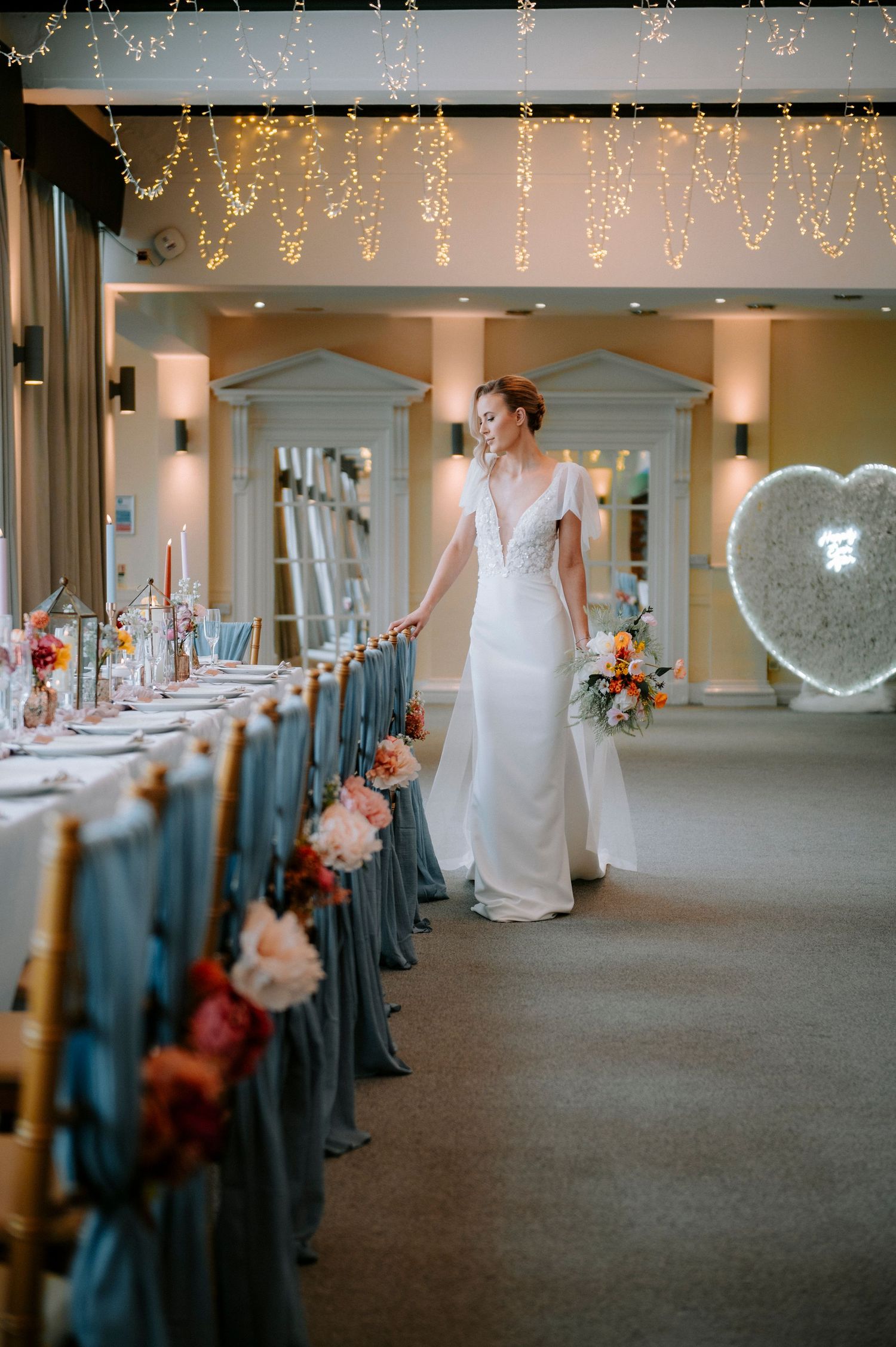 Wedding venue decorated with hanging fairy lights and teal chair covers creates a romantic atmosphere.