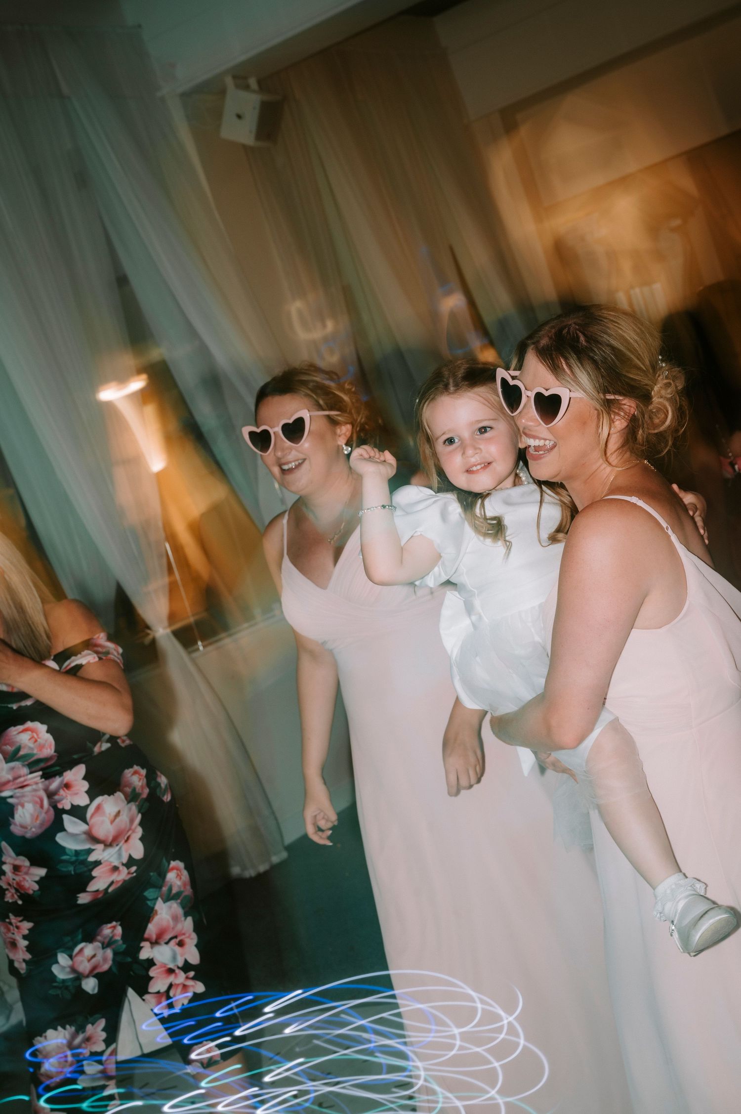Young attendants in white dresses dance and play with light trails at a reception.