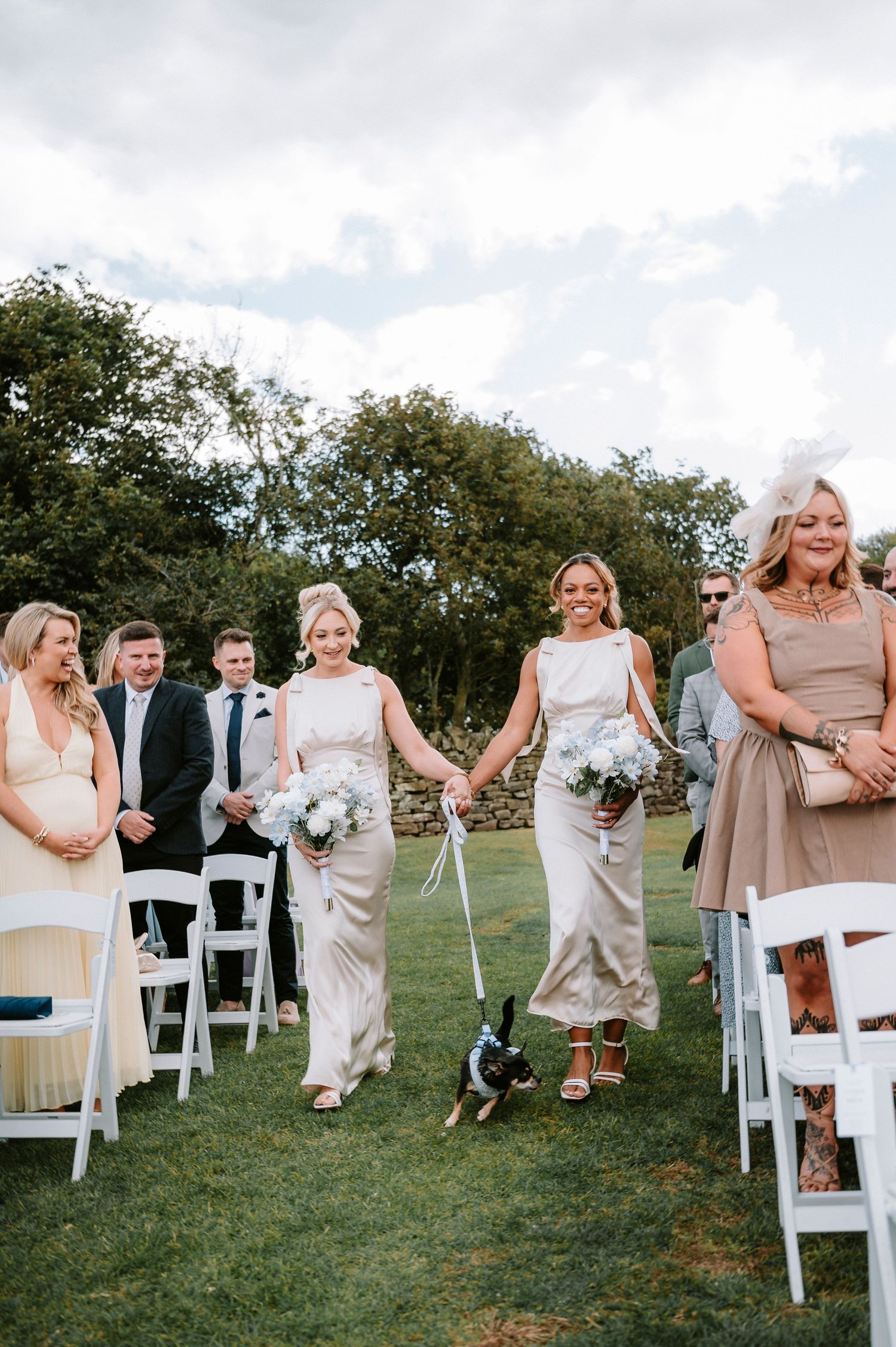 Wedding guests seated in white chairs on a grassy lawn at an outdoor ceremony.