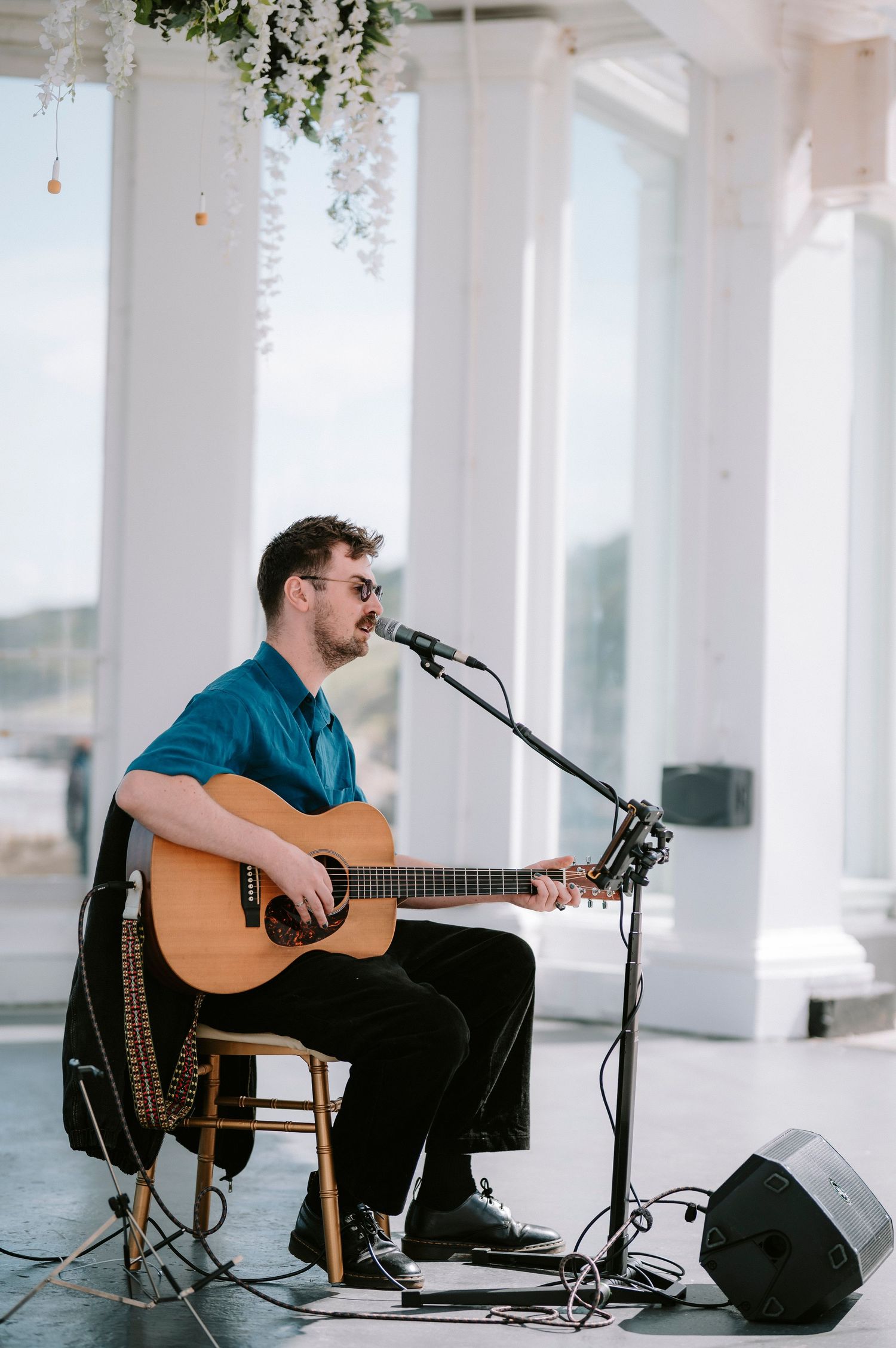 Acoustic guitarist performing at outdoor wedding venue with white pillars.
