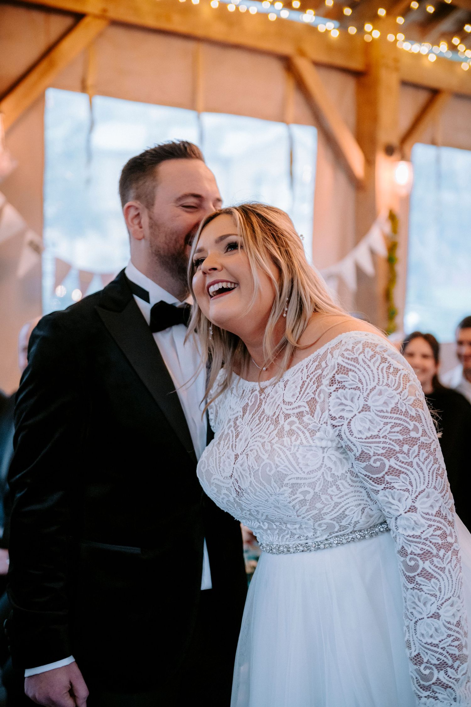 A candid moment of joy during a wedding ceremony in a rustic barn with twinkling lights.