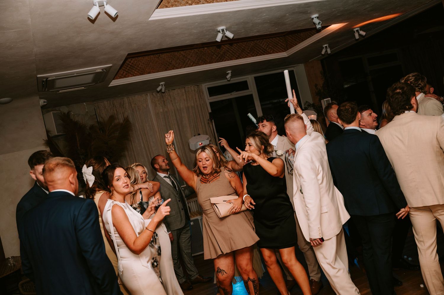 Wedding guests dancing and celebrating on a dimly lit dance floor during an evening reception celebration.