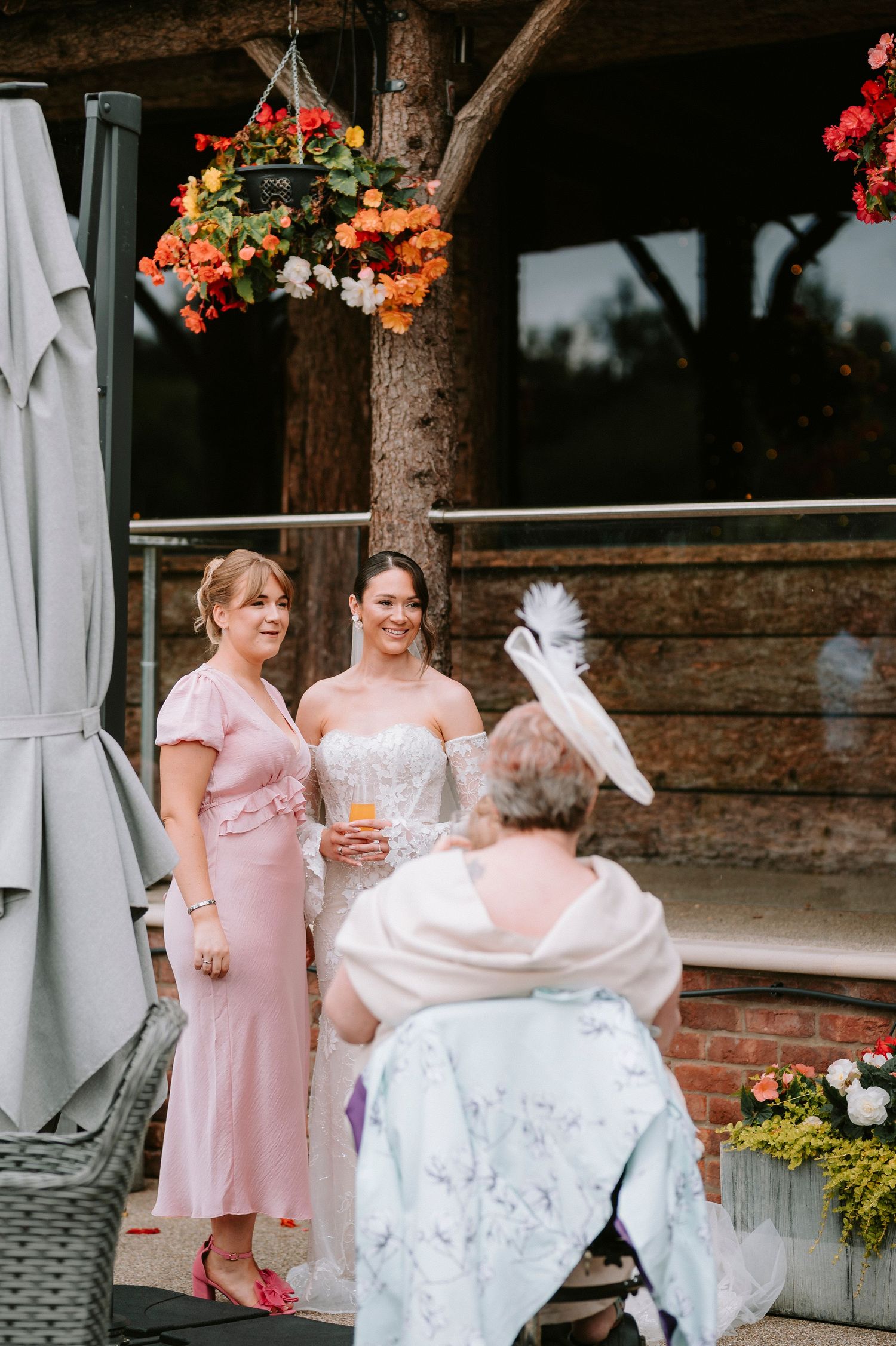 Wedding party members in pink dresses relax on outdoor patio furniture.