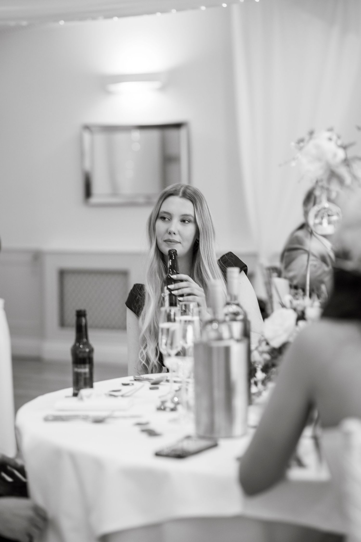 Wedding reception guests enjoying dinner at round tables with white linens and floral centerpieces.