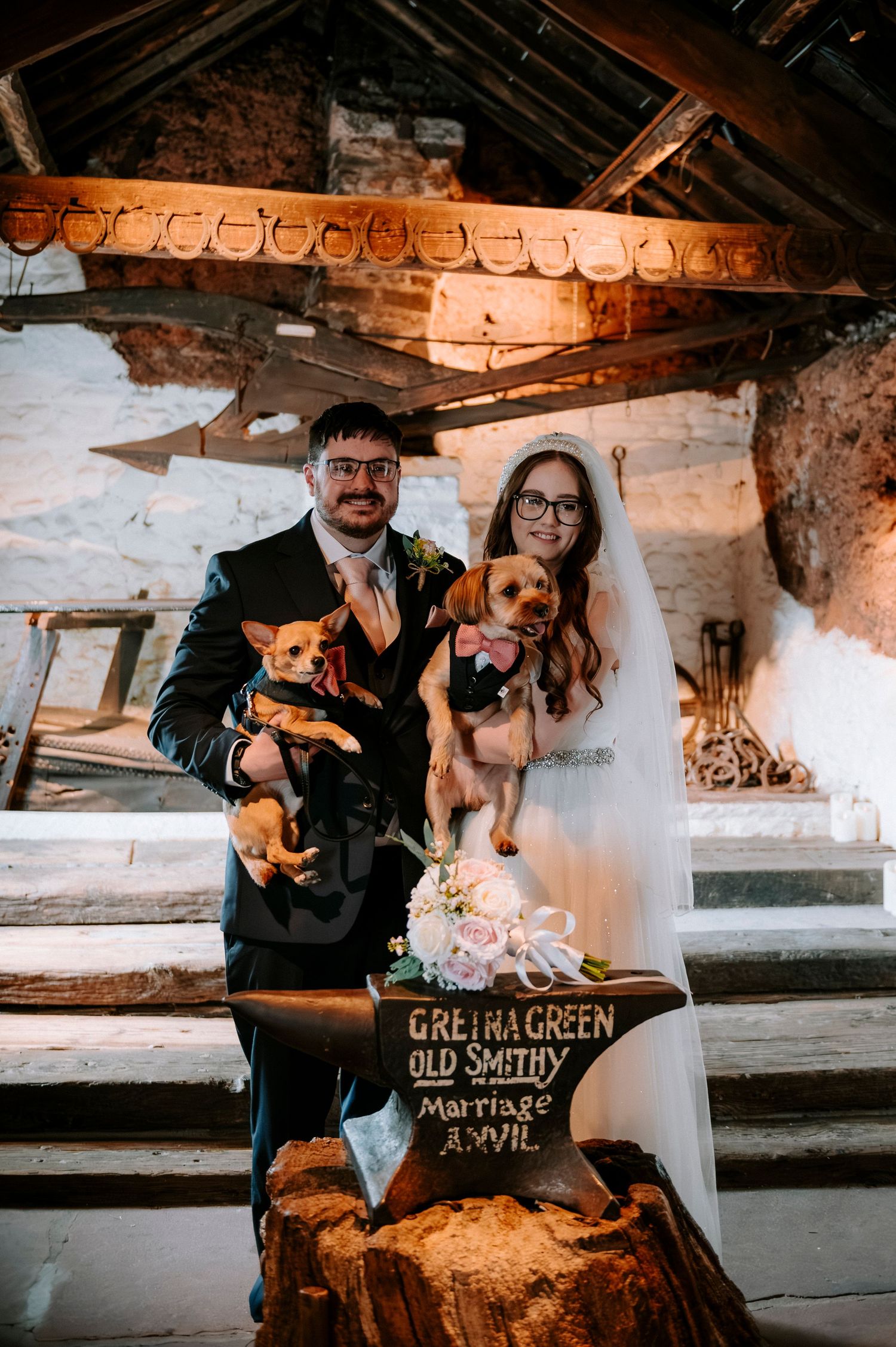 A wedding portrait with two small dogs at the historic Gretna Green anvil.