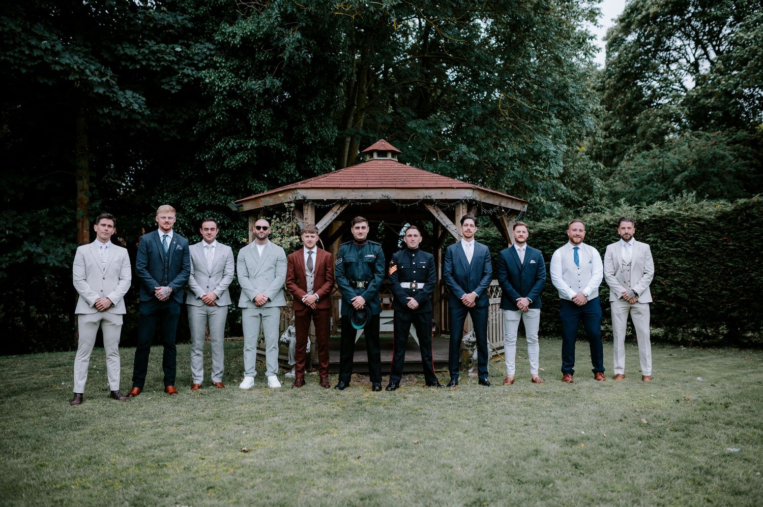 Large wedding party group photo lined up under gazebo in formal attire.