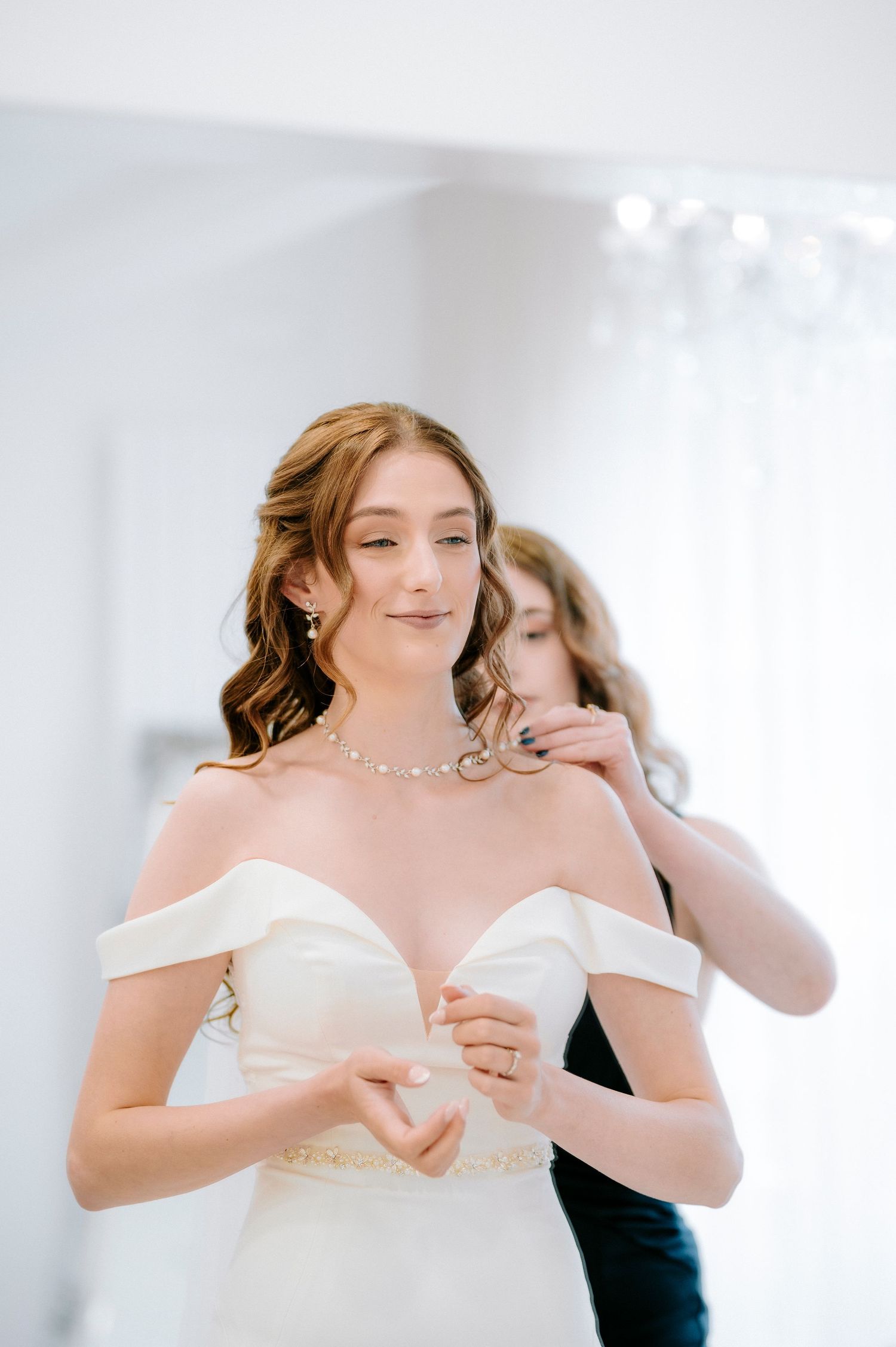 Bride in white off-shoulder gown getting ready with bridesmaids.
