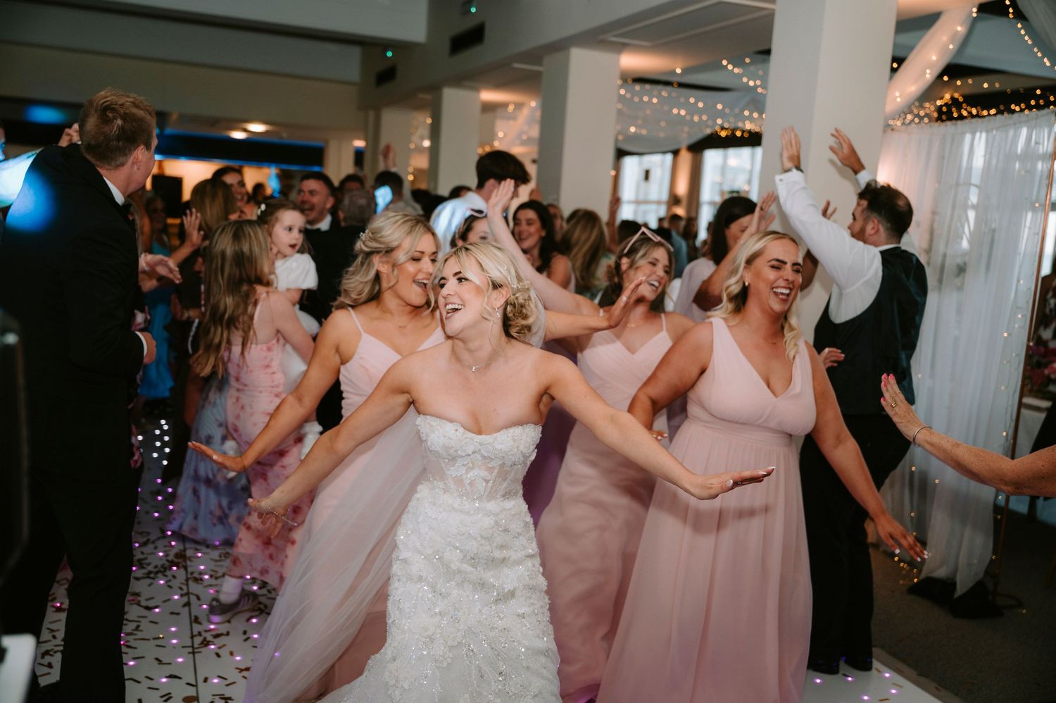 Wedding party in pink bridesmaid dresses dancing together at the reception.