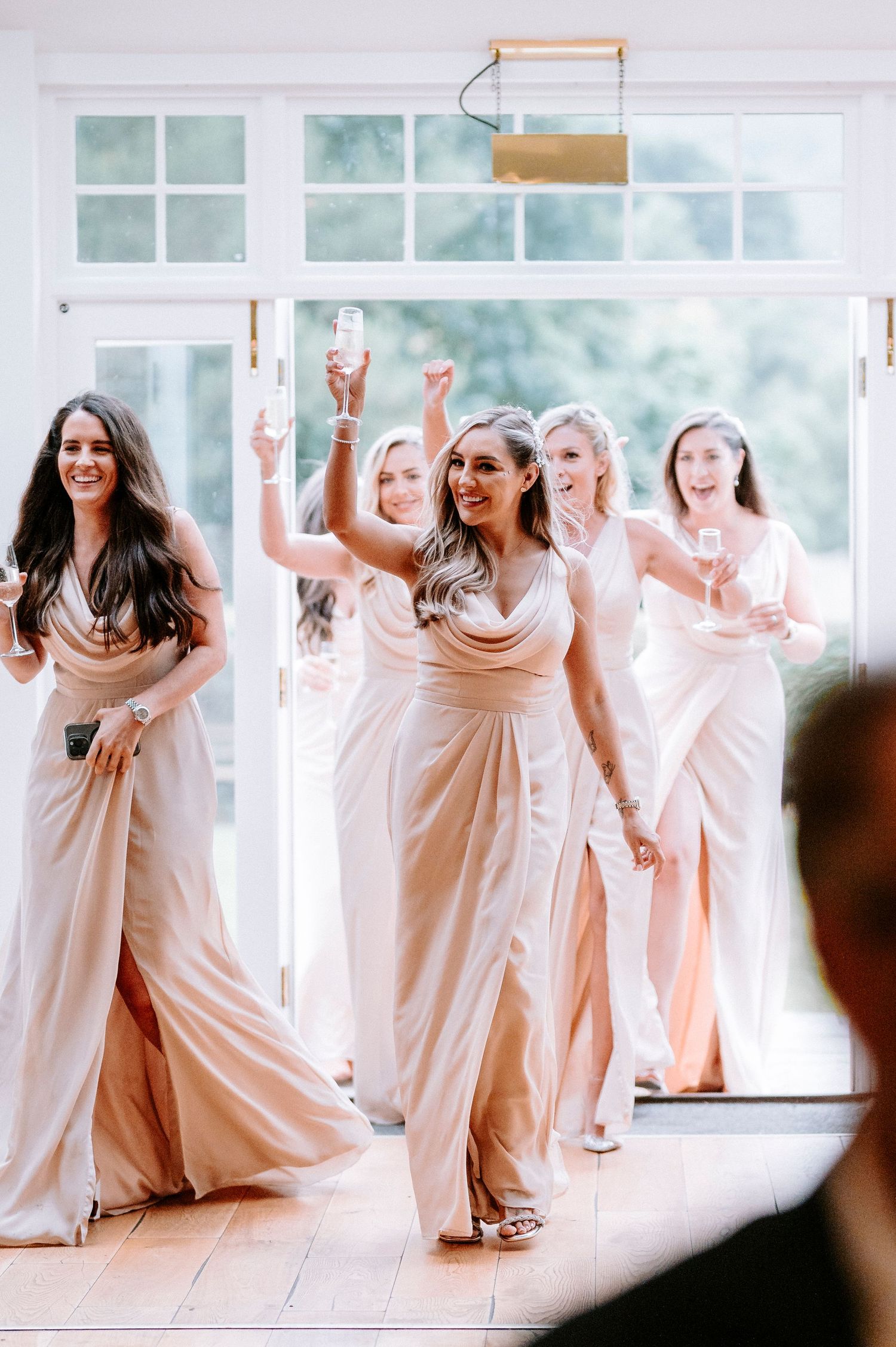 Bridesmaids in blush pink dresses dance and celebrate during a wedding reception.