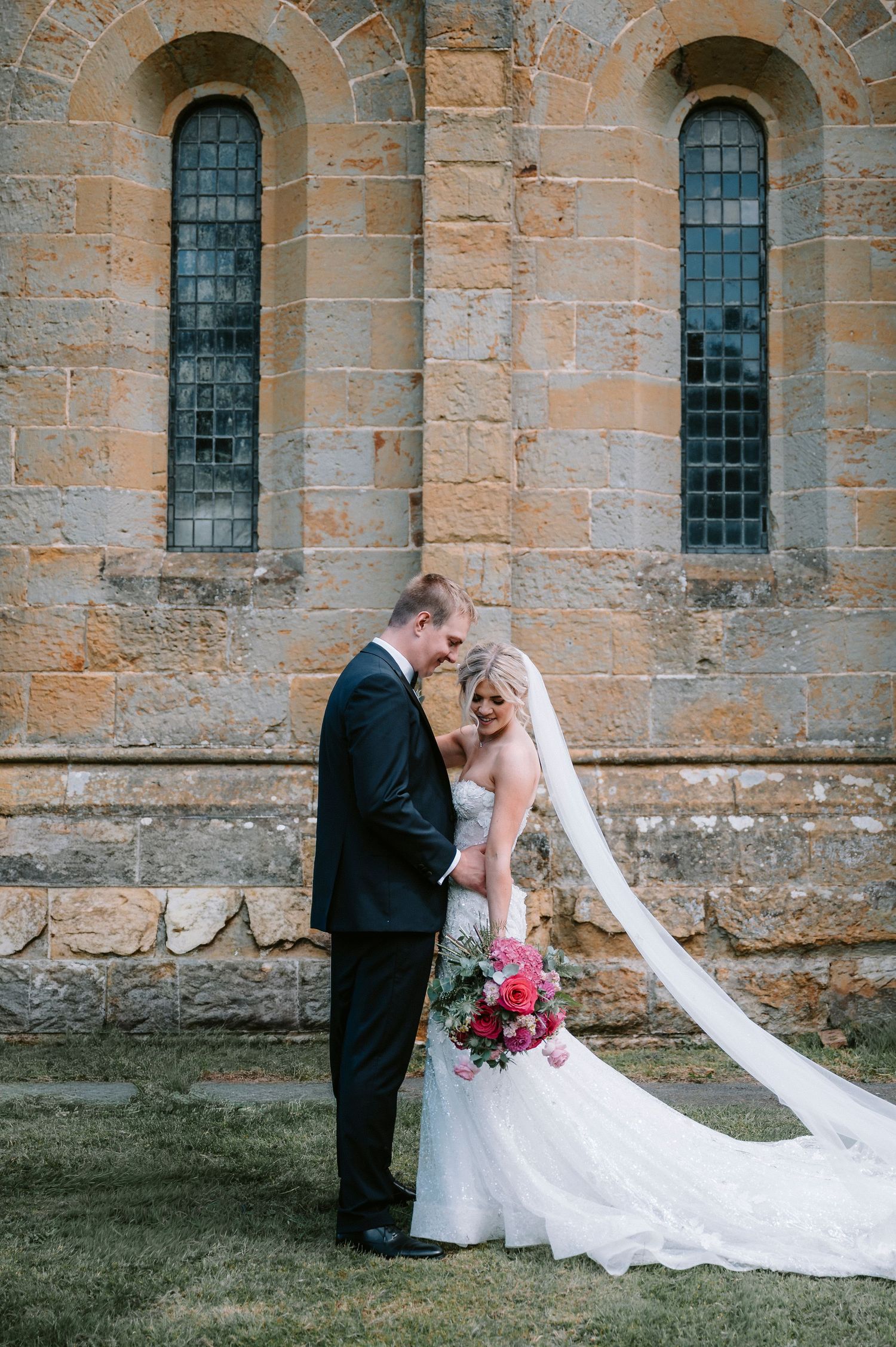 Romantic wedding portrait by sandstone church with long flowing veil.