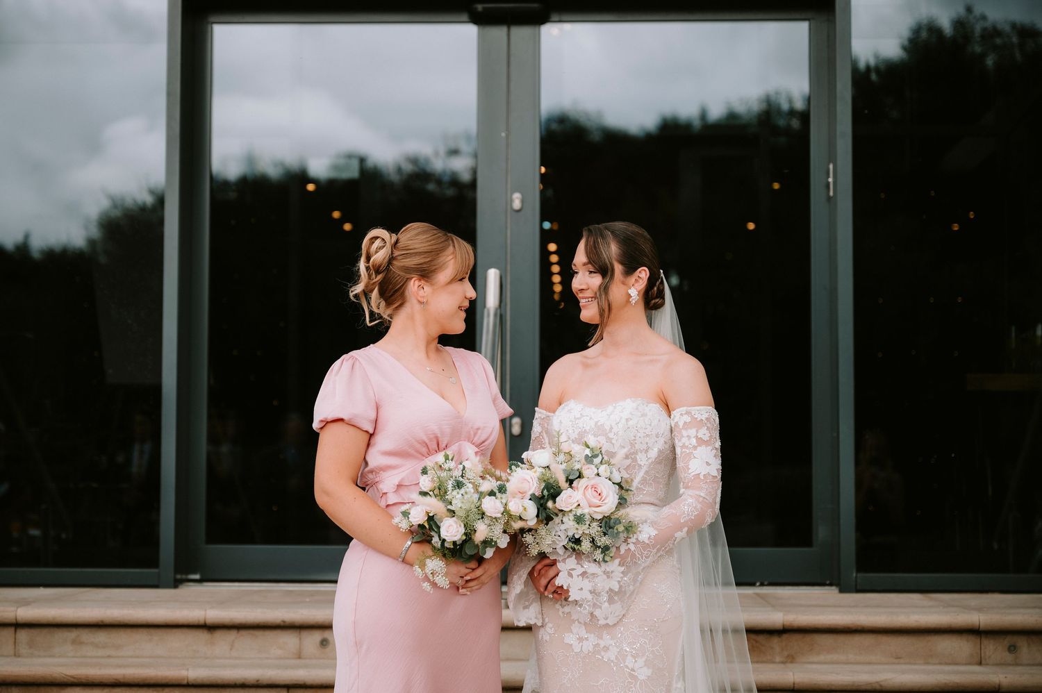 Wedding party members in pink dresses holding white floral bouquets outdoors.