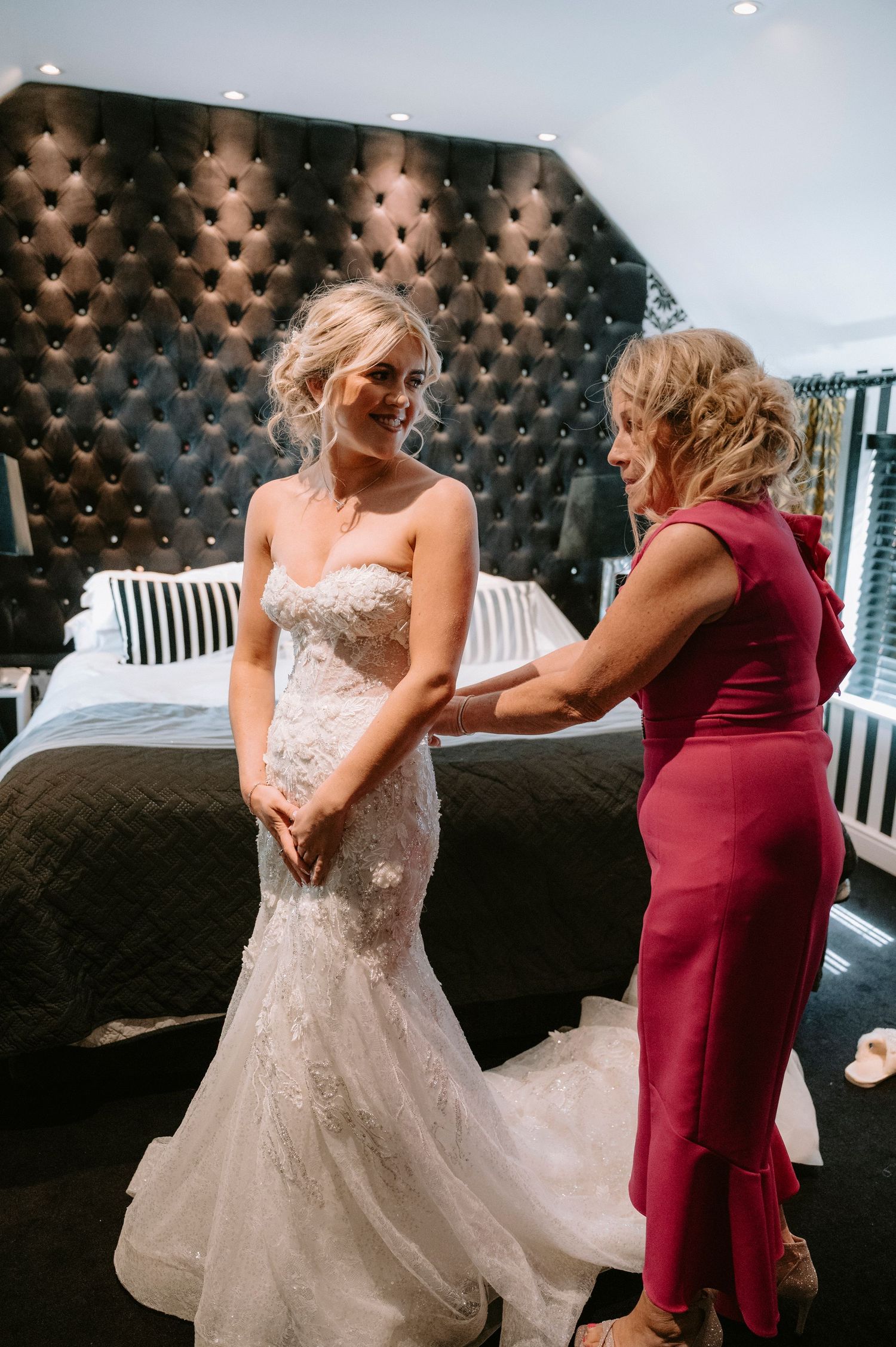 Bride in a lace gown sharing playful dance moves with someone in burgundy.