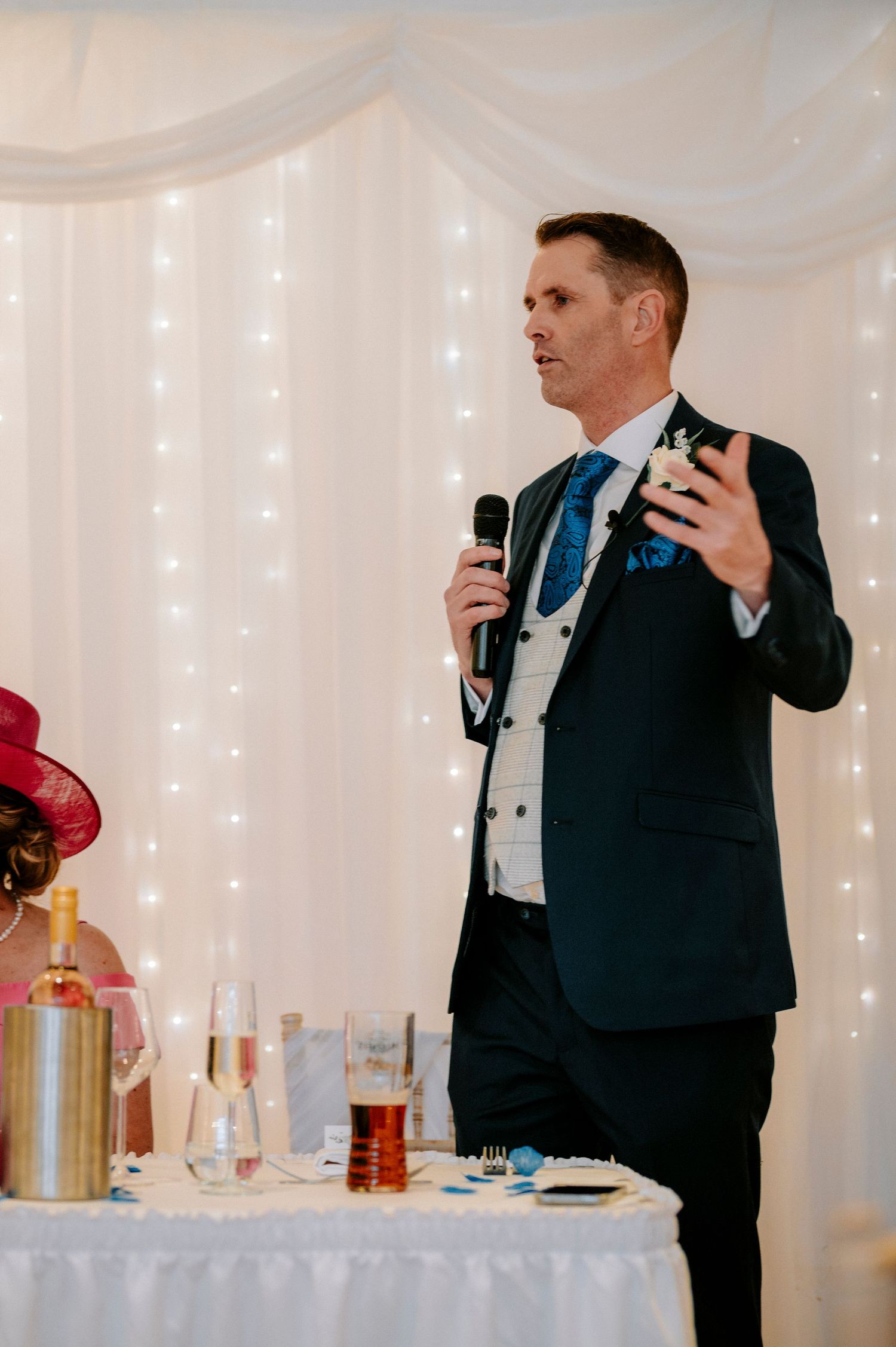 Wedding reception speech being given in an elegant white-draped venue with twinkle lights.