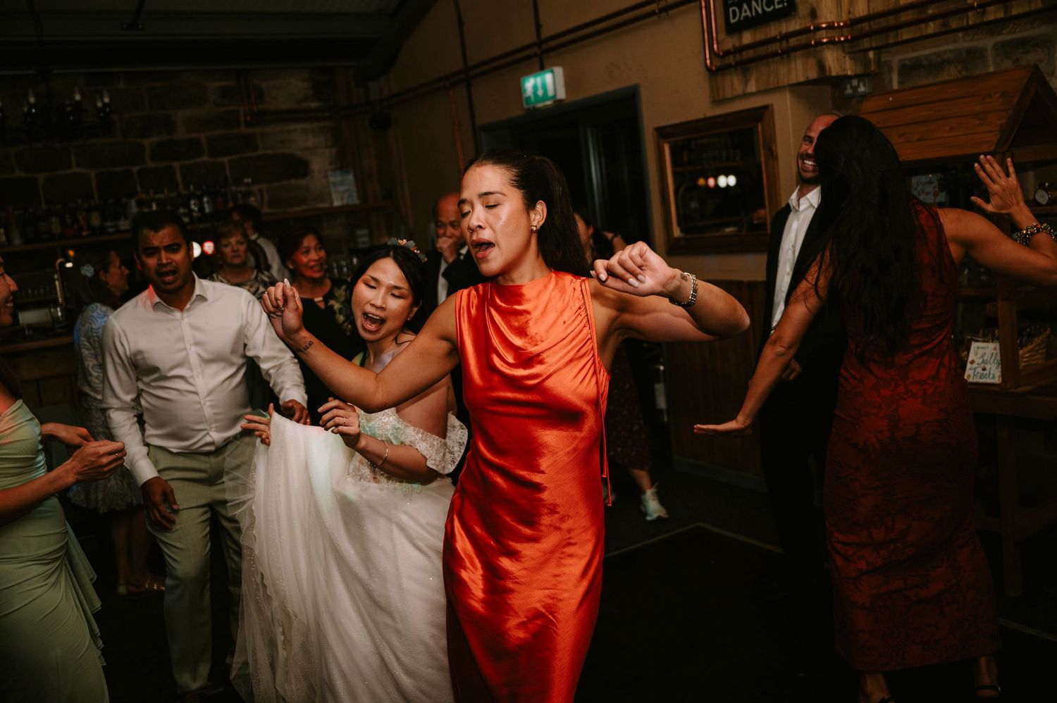 Wedding reception dance party with guests moving energetically on a dark dance floor.