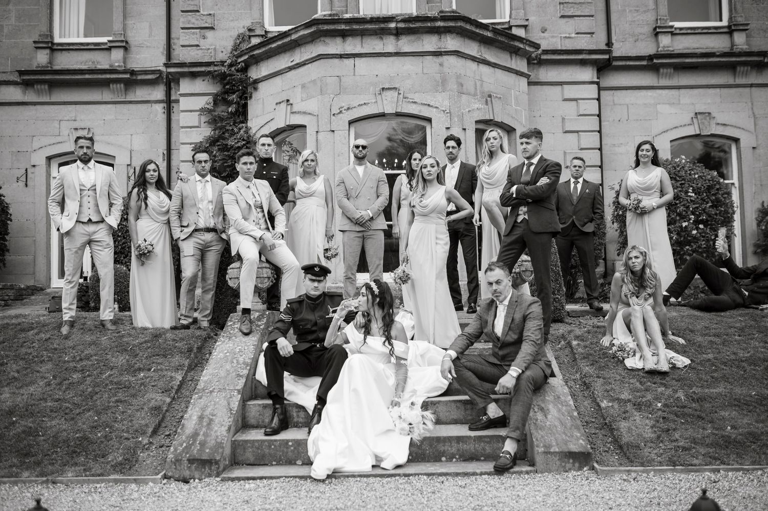 A vintage black and white wedding group photo taken in front of a historic stone building.