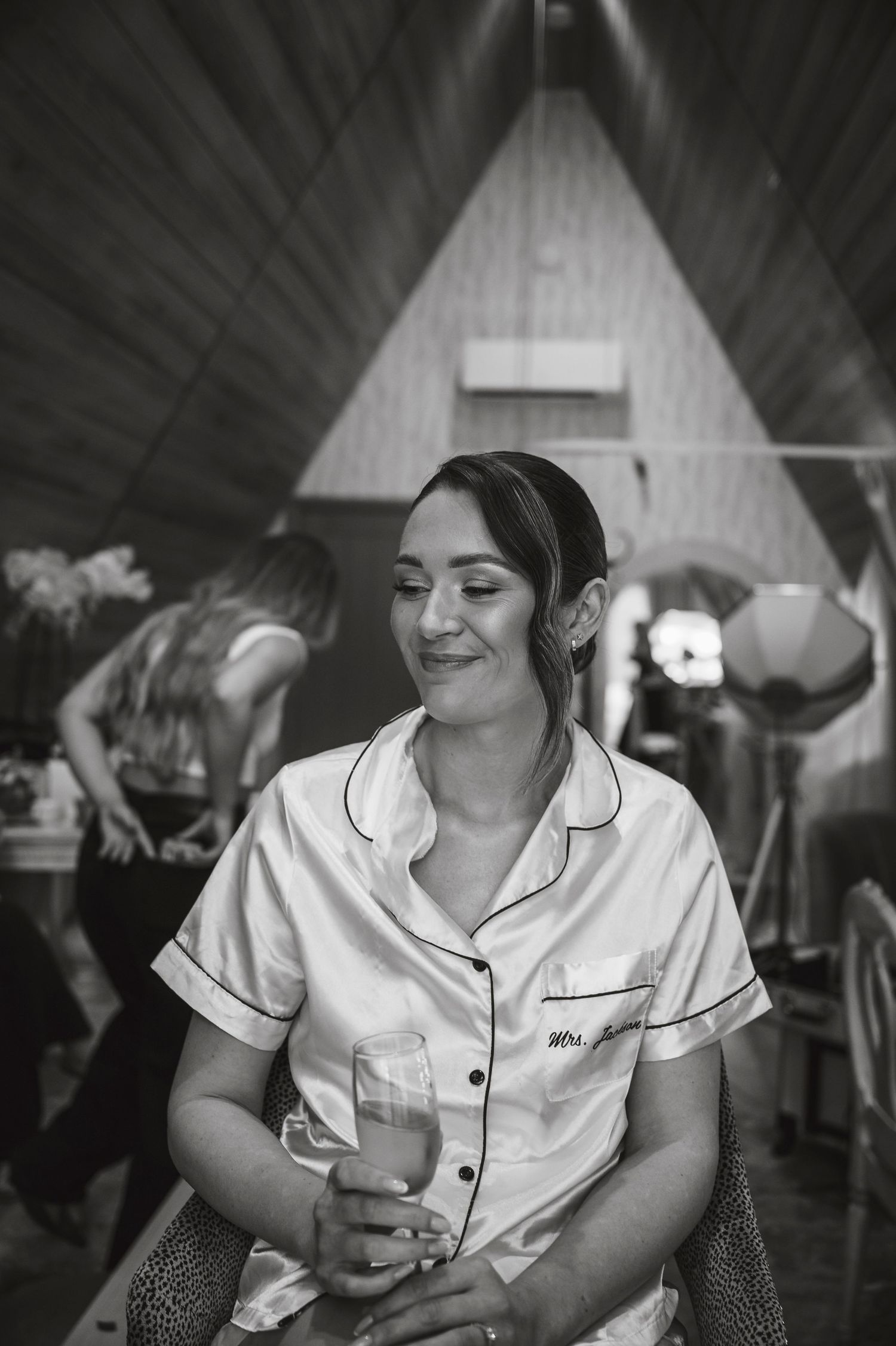 Person in white satin pajamas relaxing in a dimly lit room during wedding preparations.