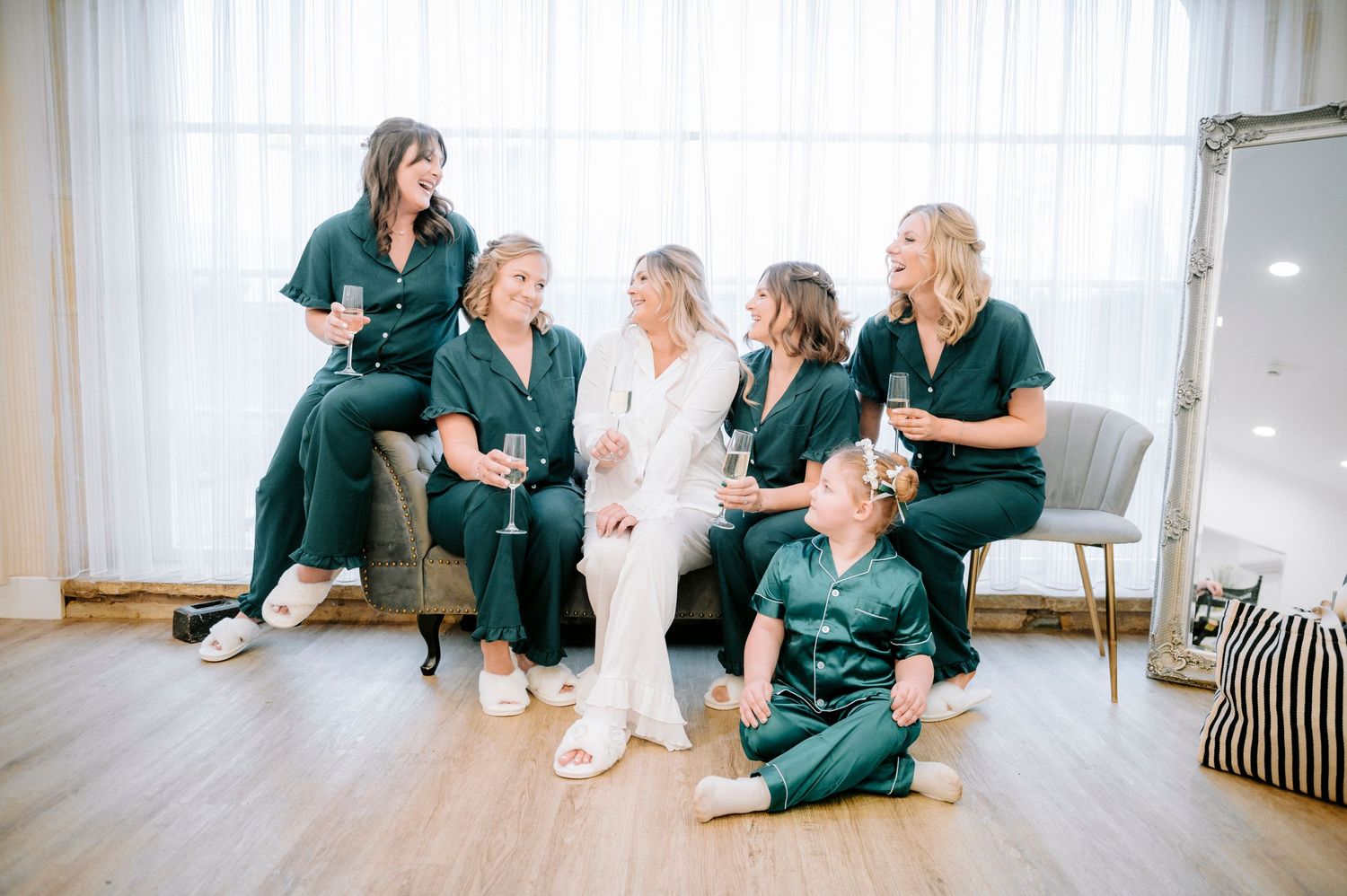 Bridal party in emerald green robes relaxes on floor during wedding preparations.