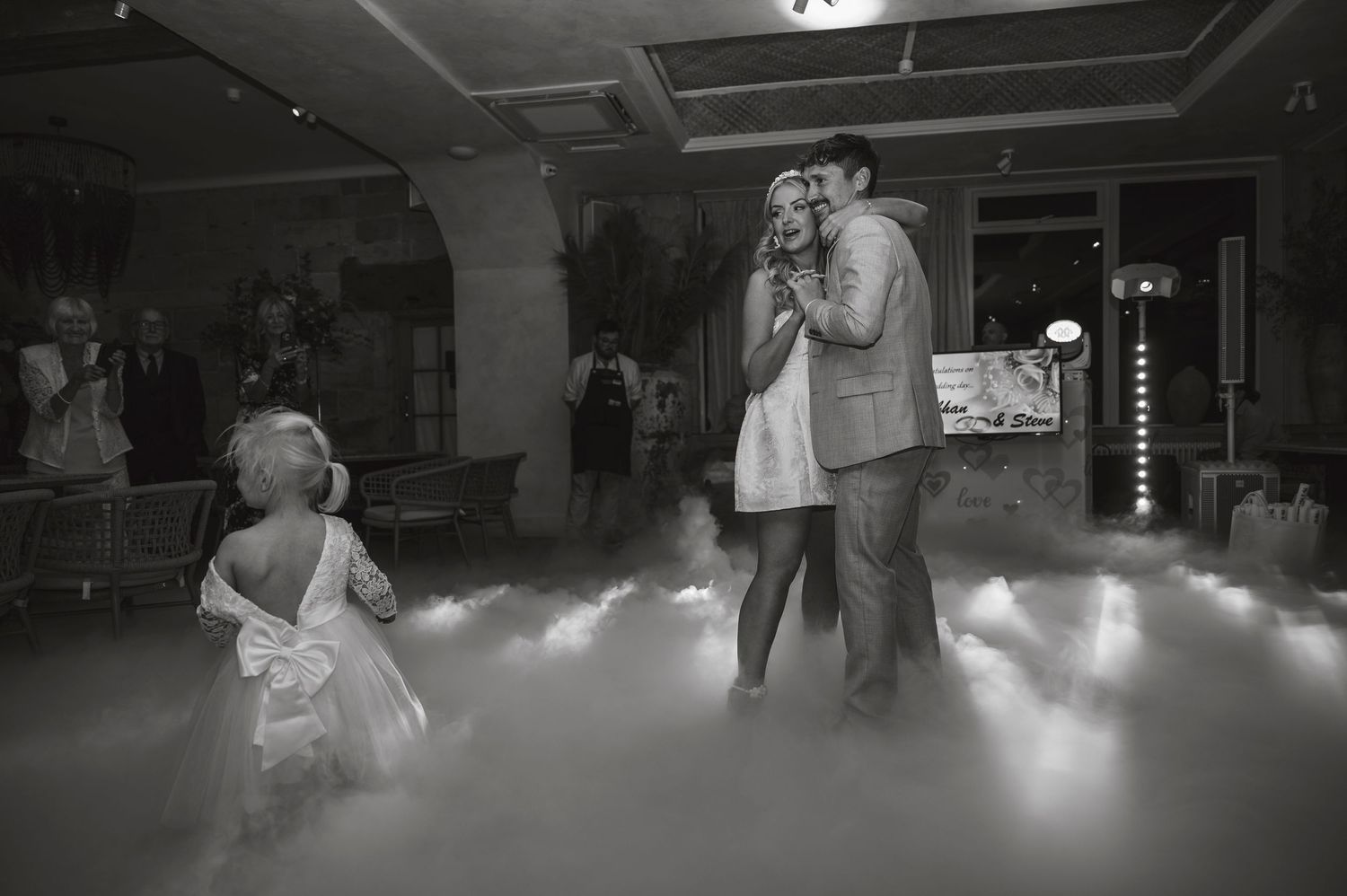 Wedding couple dancing in a dark reception venue with atmospheric fog on the dance floor.