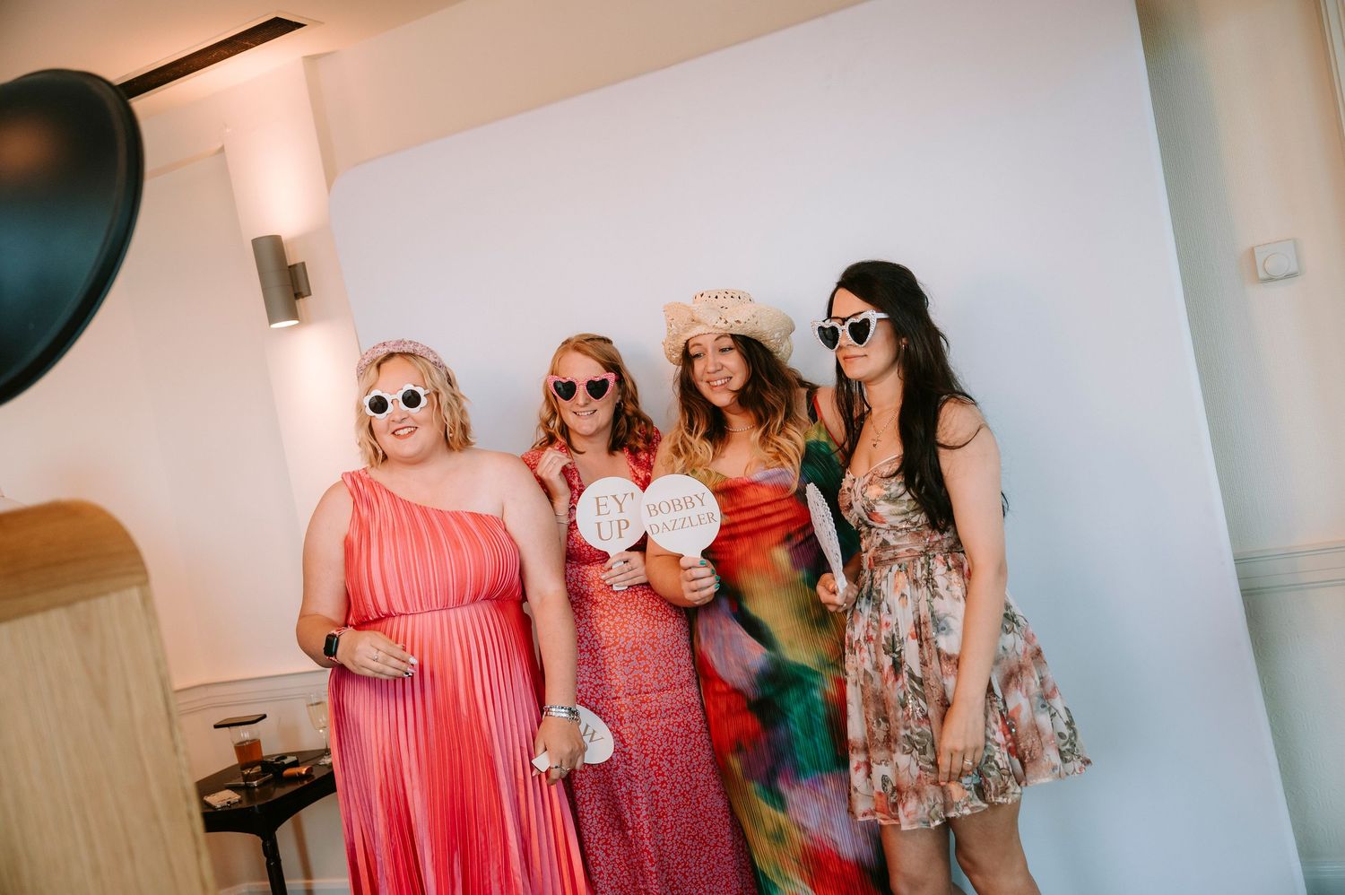 Wedding party wearing sunglasses and coral dresses pose together indoors.