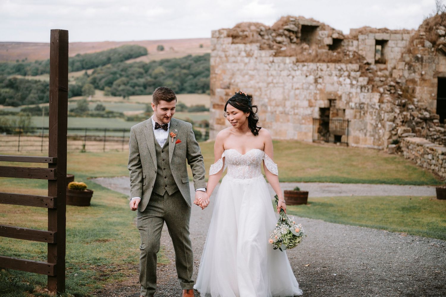 Couple walking along path at historic castle ruins with countryside views.