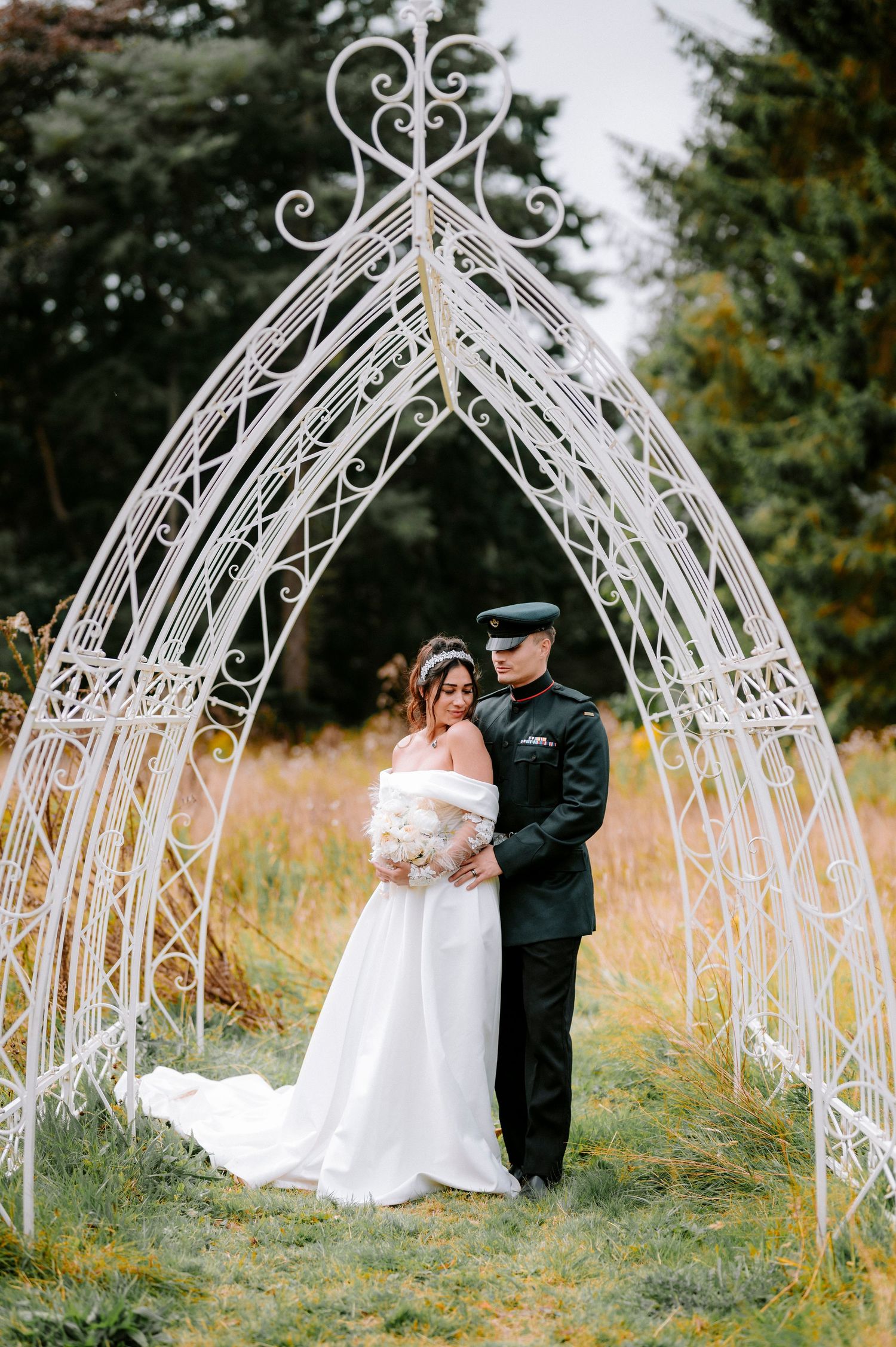 A romantic wedding photo sequence under an ornate white metal garden arch in an outdoor setting.
