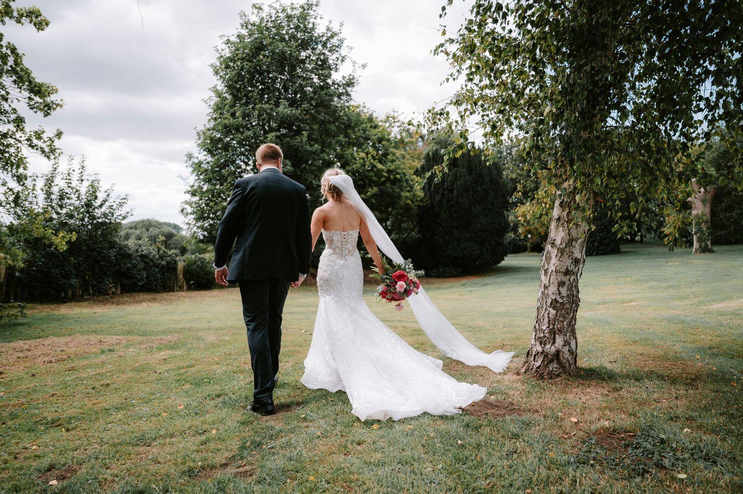 Couple walks across scenic grassy field during wedding photoshoot.
