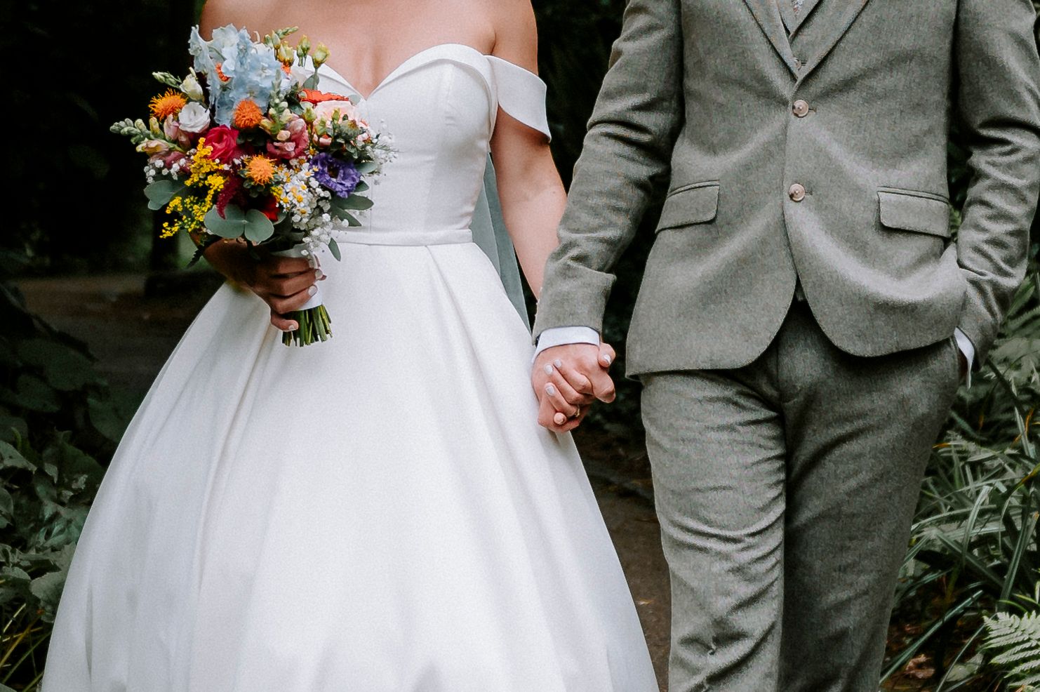 Close-up detail of wedding attire showing white dress and gray suit with colorful bouquet.