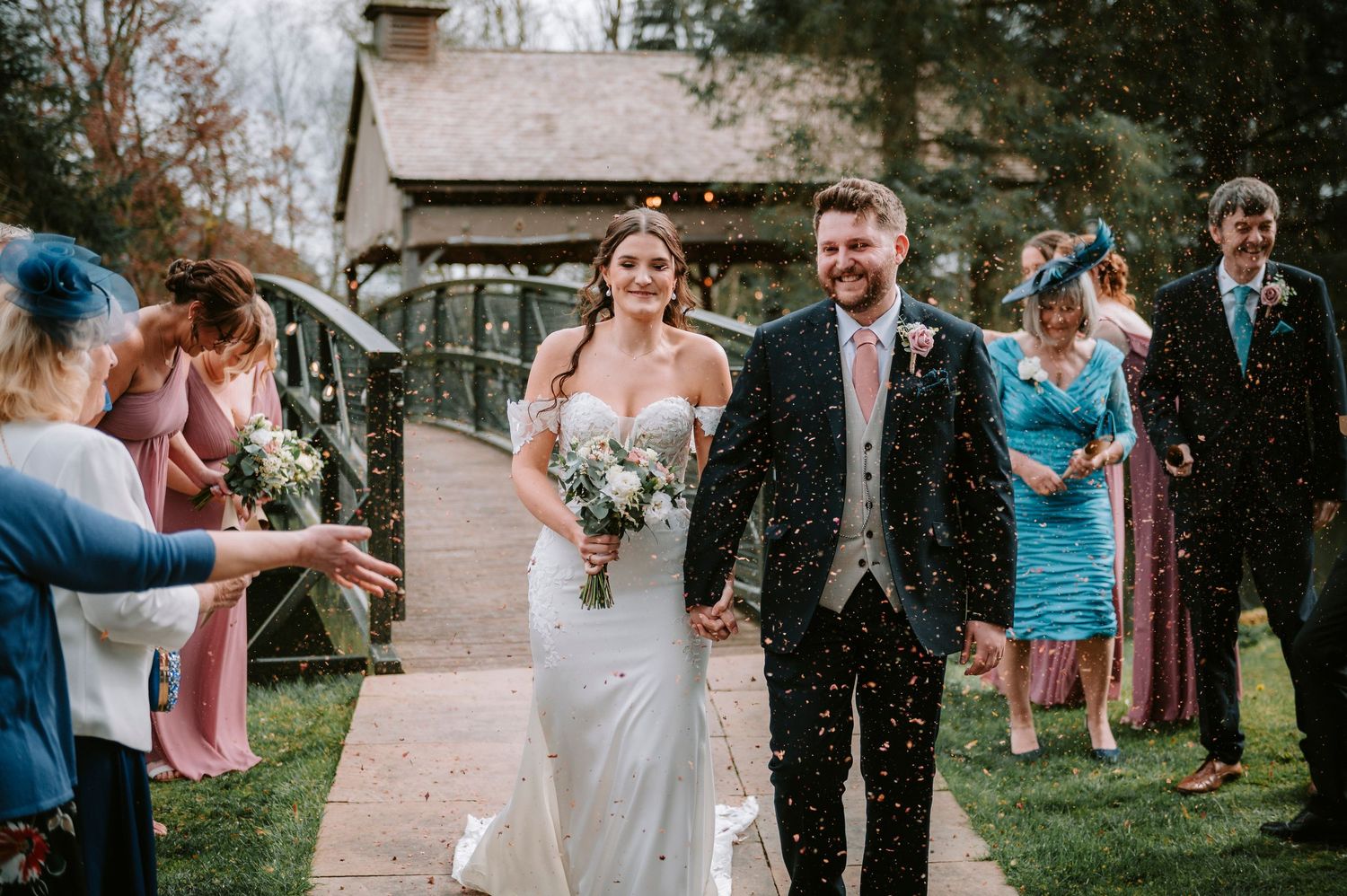 Wedding celebration with guests throwing confetti in an outdoor garden setting.