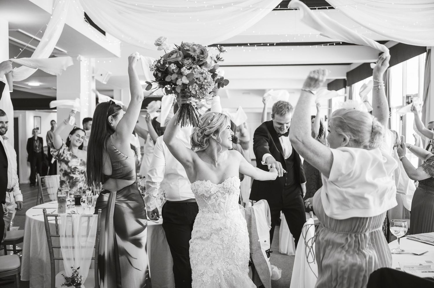 Wedding celebration with dancing guests under draped ceiling decorations.